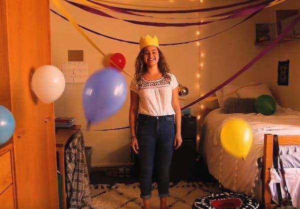 Woman in a crown smiles, posing in a decorated bedroom with balloons.