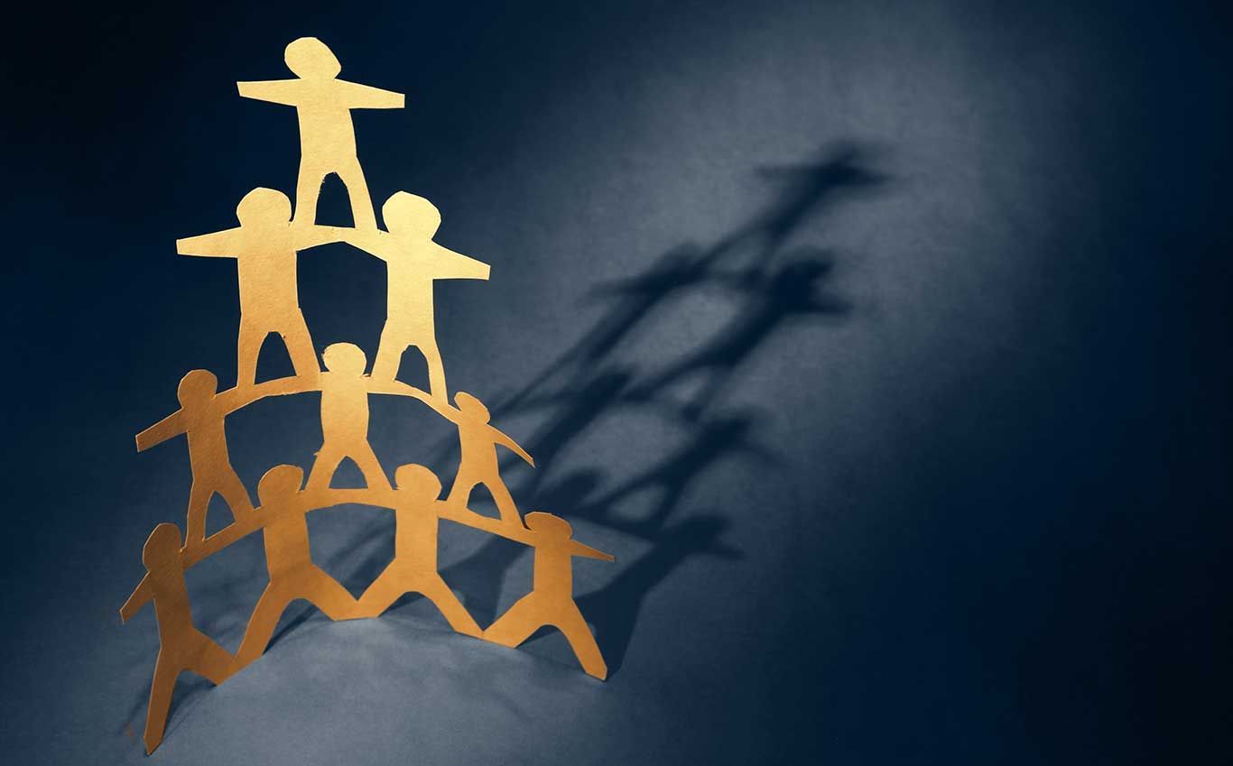 Golden paper figures forming a human pyramid with a dark blue backdrop.