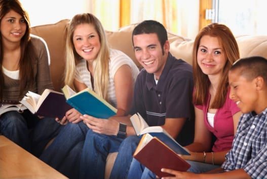 Group of teens reading books on a couch; smiling and looking at the camera.