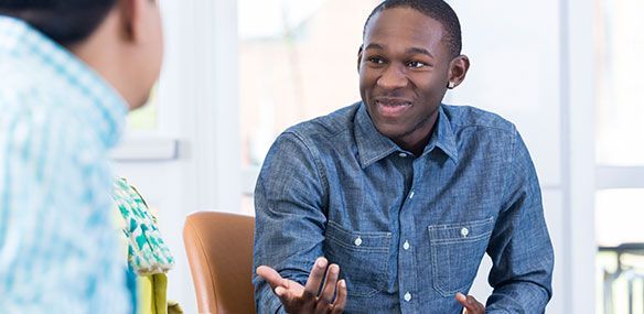 Man in blue shirt gesturing and smiling while talking with another person.