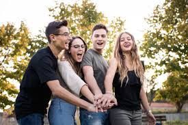 Four young people with hands stacked, smiling outdoors.