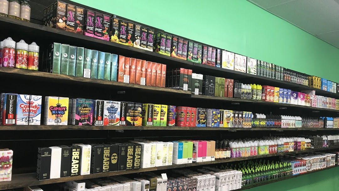 Shelves stocked with various vape juice bottles and boxes in a store against a green wall.