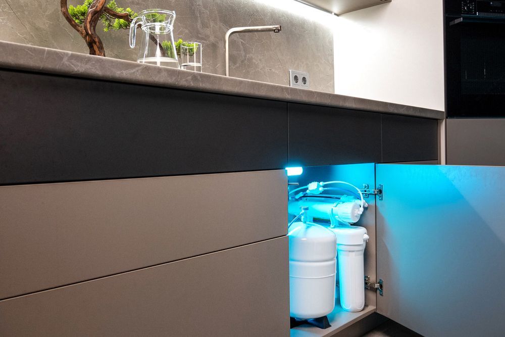 Modern kitchen with under-sink cabinet open, showing illuminated cleaning supplies and plumbing.