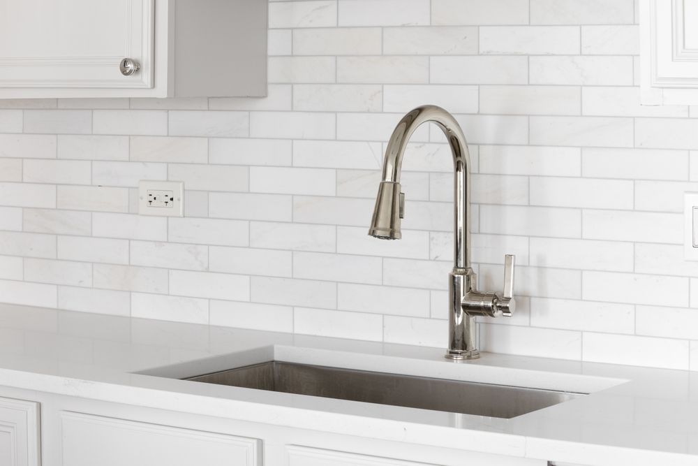 Modern white kitchen with stainless steel sink and tall chrome faucet against a white tile backsplash