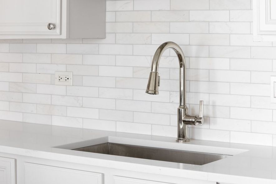 Modern white kitchen with stainless steel sink and tall chrome faucet against a white tile backsplash