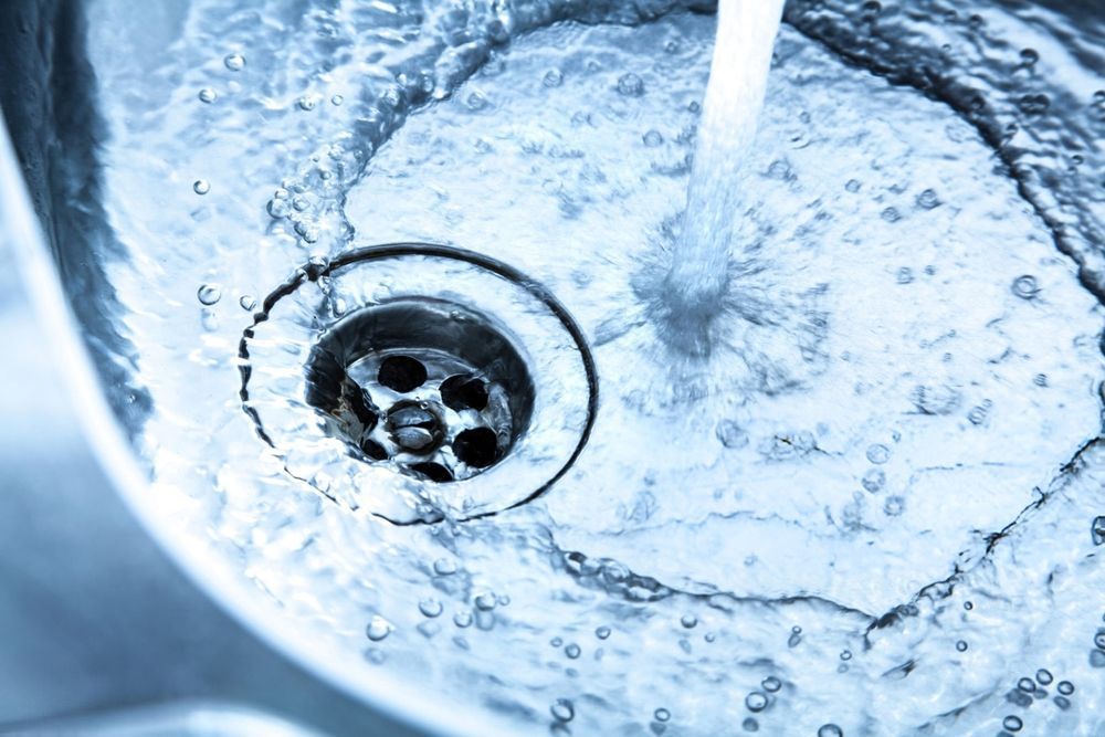 Water flowing into a stainless steel sink drain with swirling bubbles.