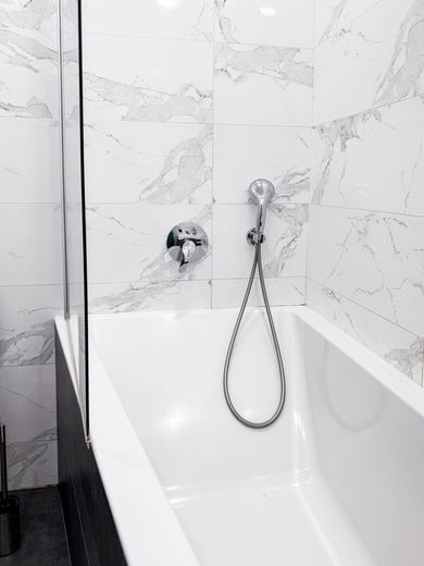 Modern white bathroom with a freestanding tub and handheld shower against marble tile walls