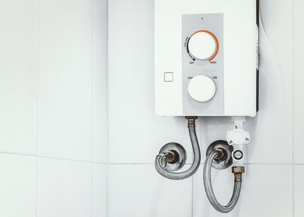 White wall-mounted water heater with dials and connected hoses in a tiled bathroom