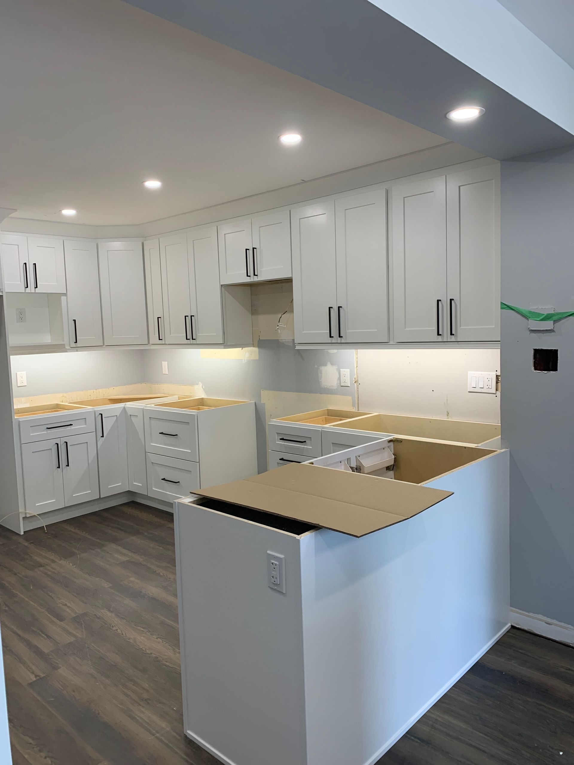 A kitchen with white cabinets and wooden floors is being remodeled.