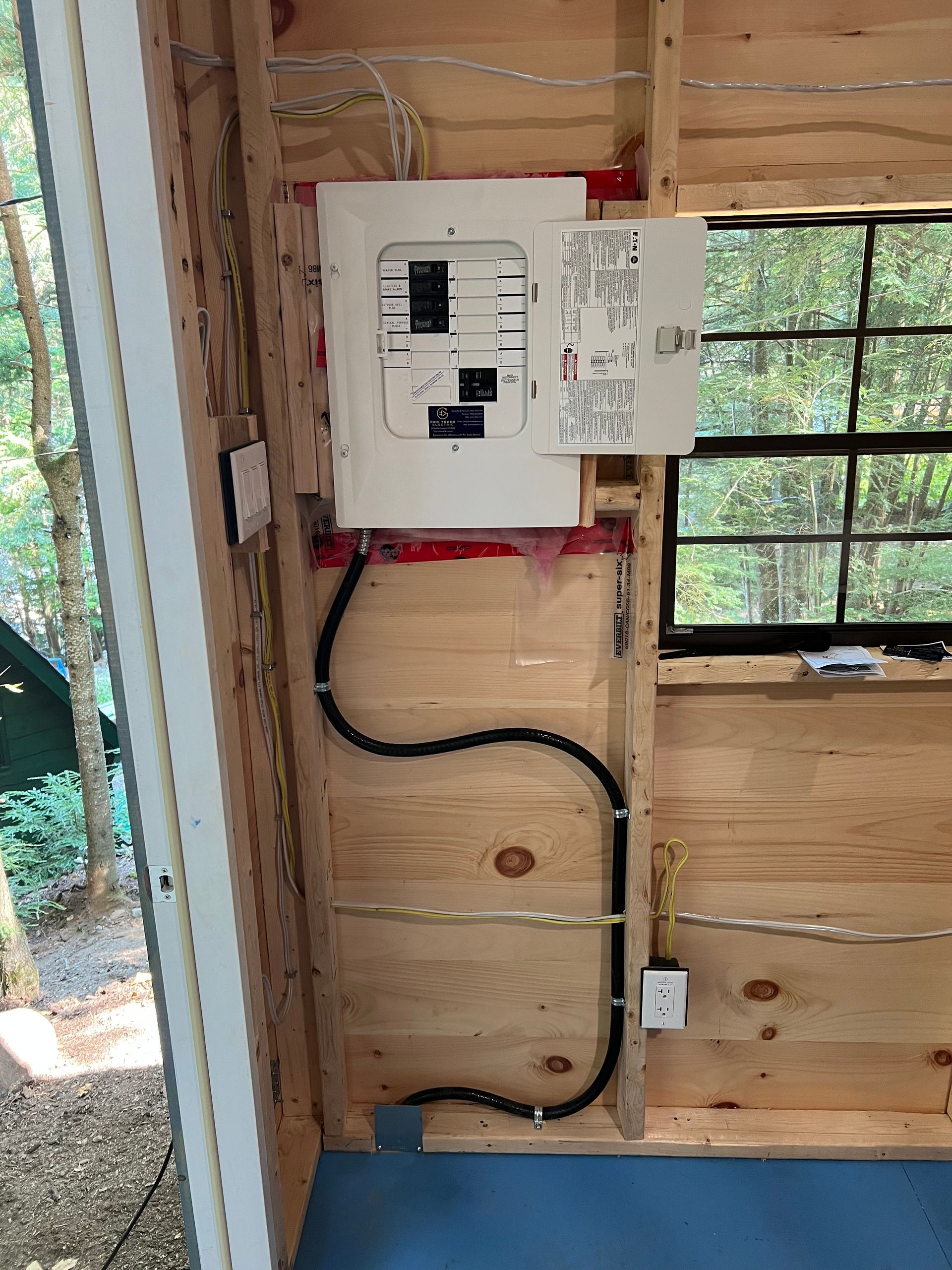 A electrical box is hanging on a wooden wall next to a window.