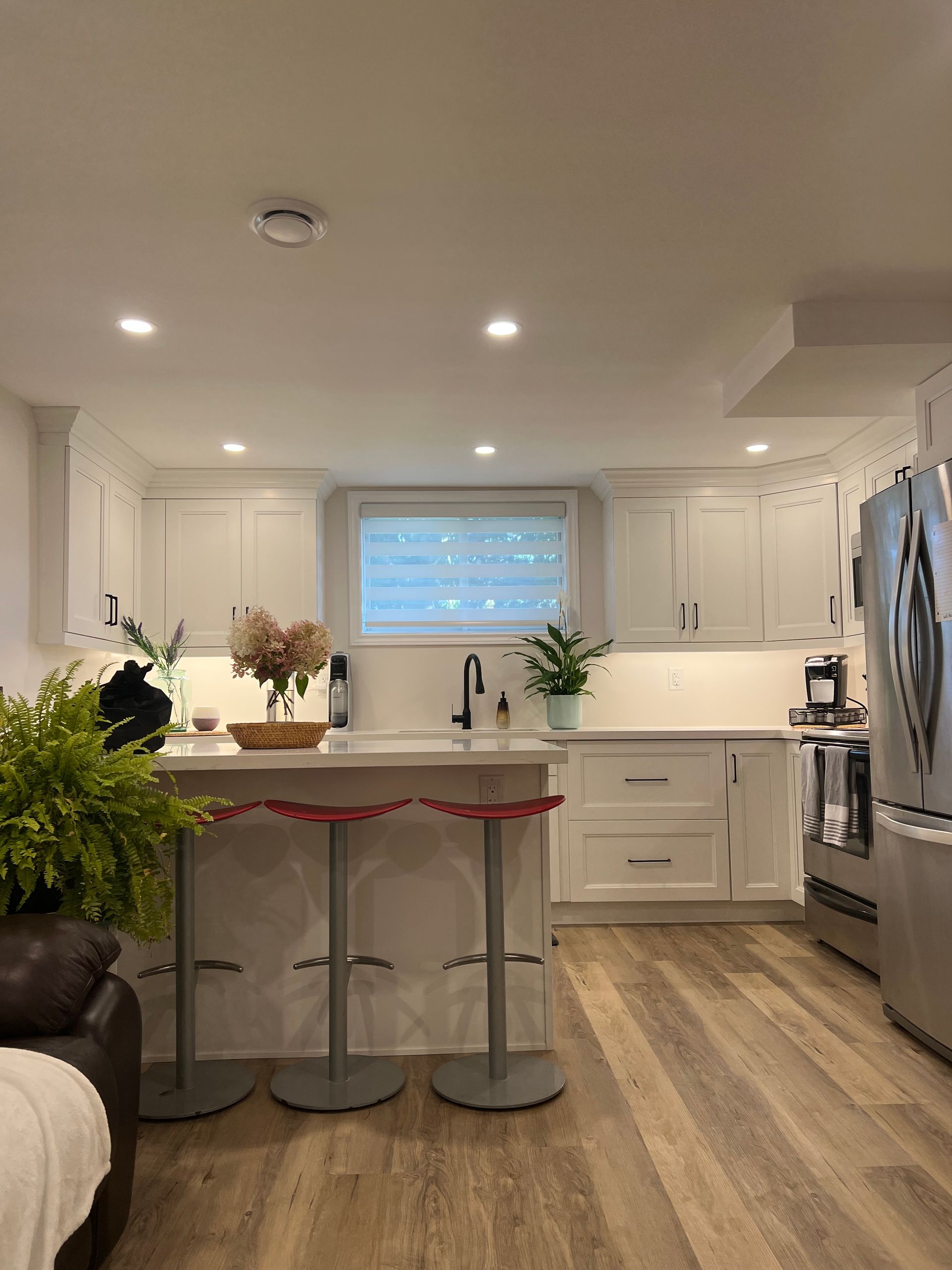 A kitchen with white cabinets , stainless steel appliances , hardwood floors and a large island.