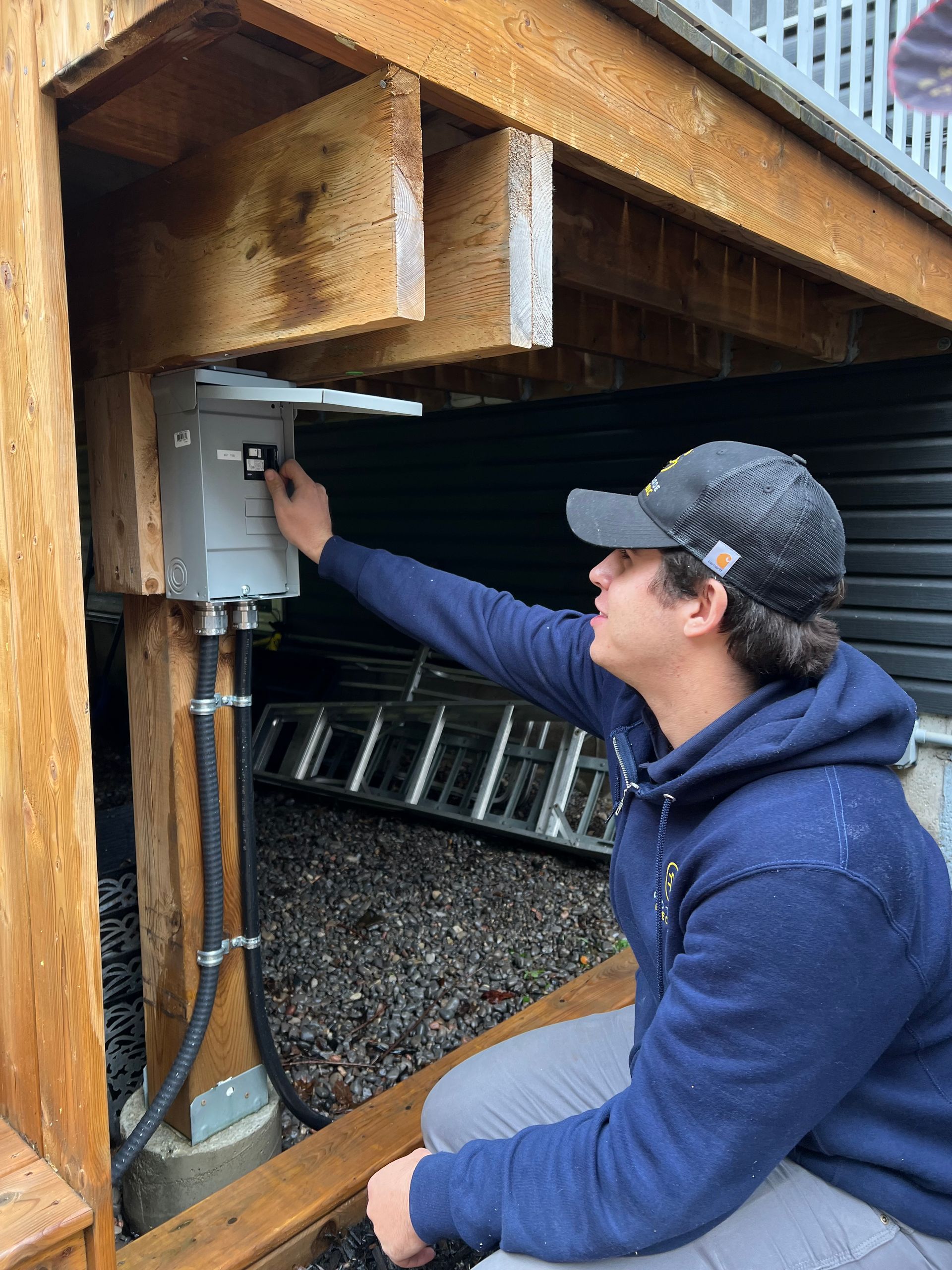 A man is working on an electrical box under a deck.