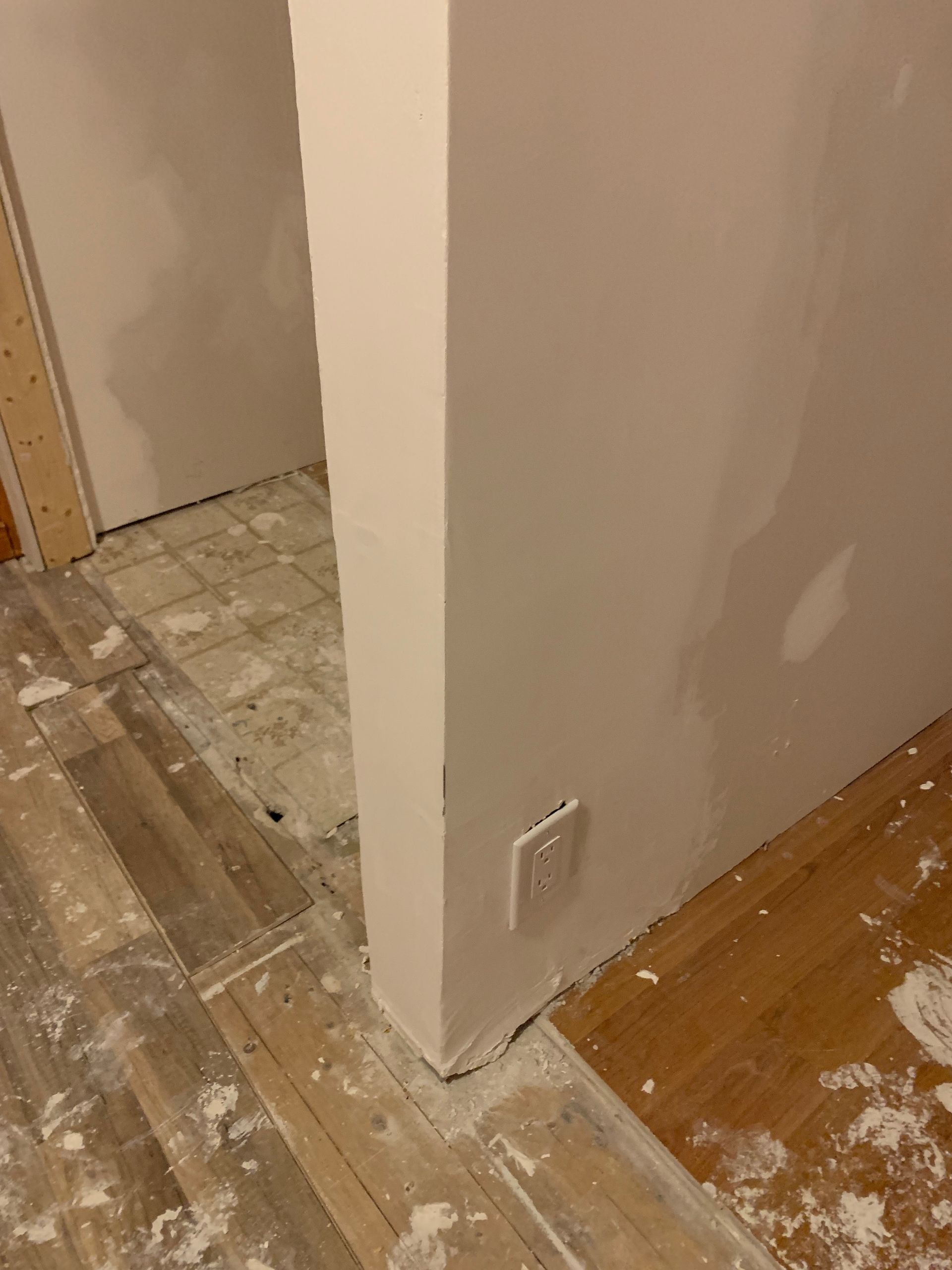 A corner of a room with a white wall and a wooden floor.