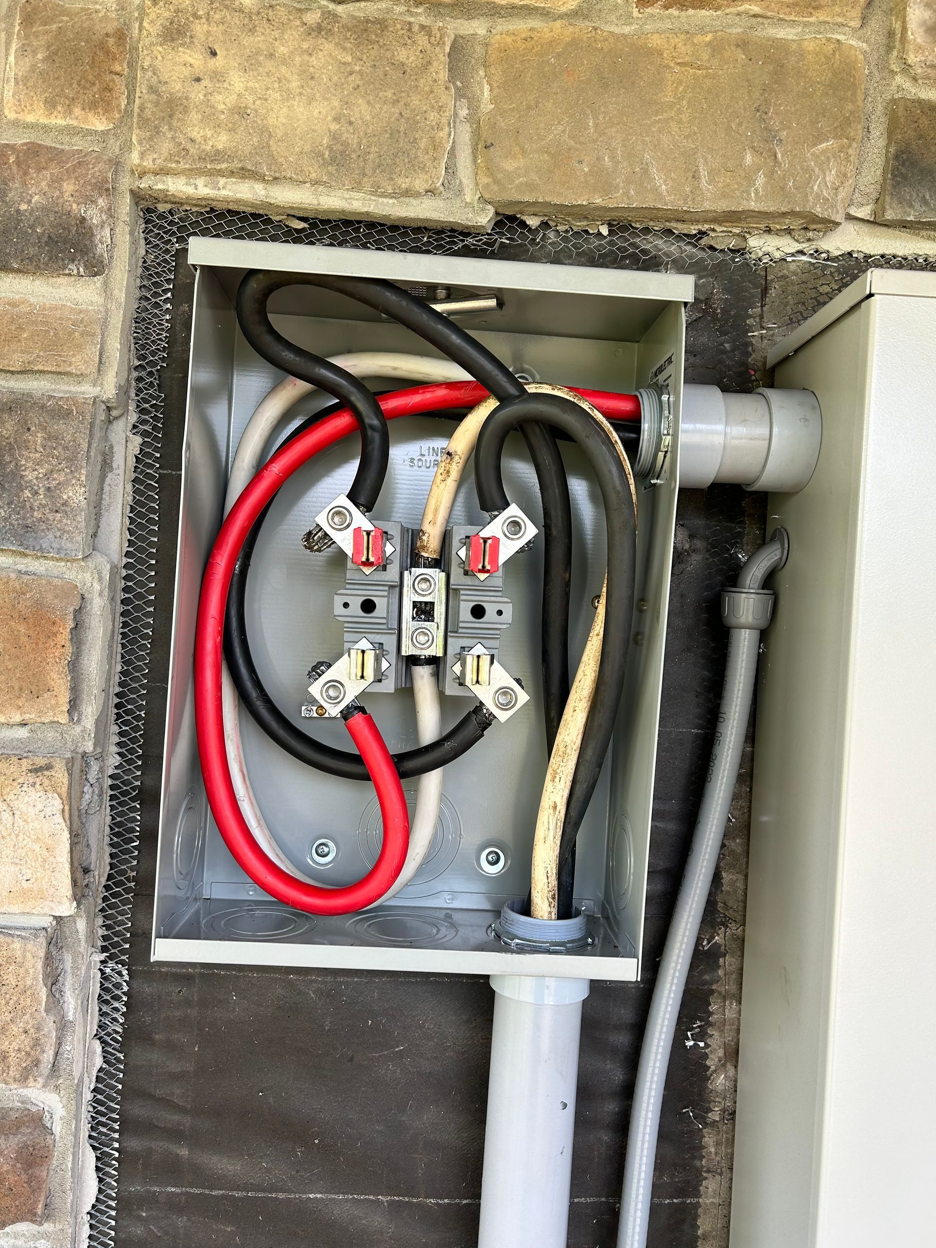 A box with wires coming out of it is attached to a brick wall.