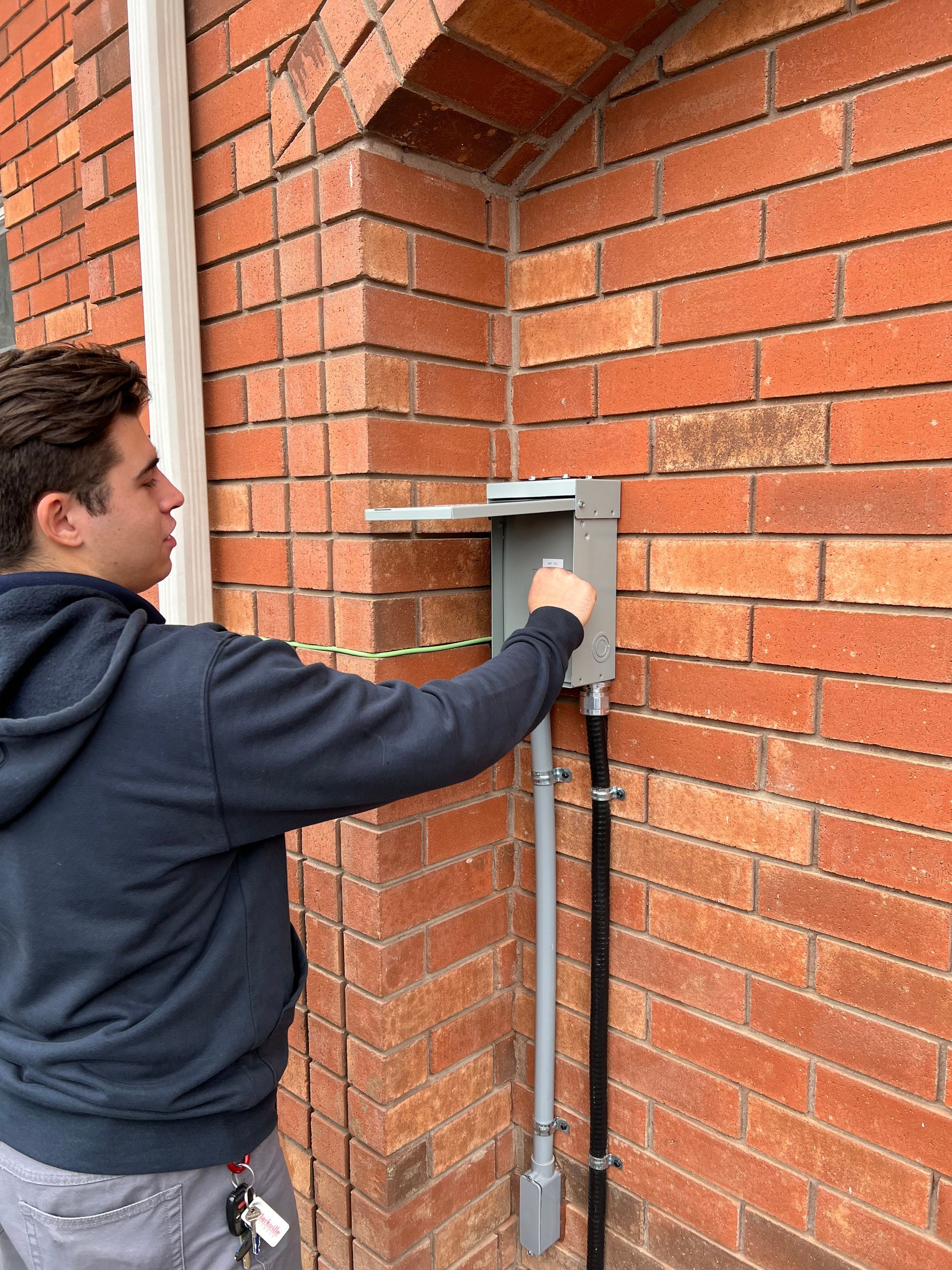 A man is working on an electrical box on a brick wall.