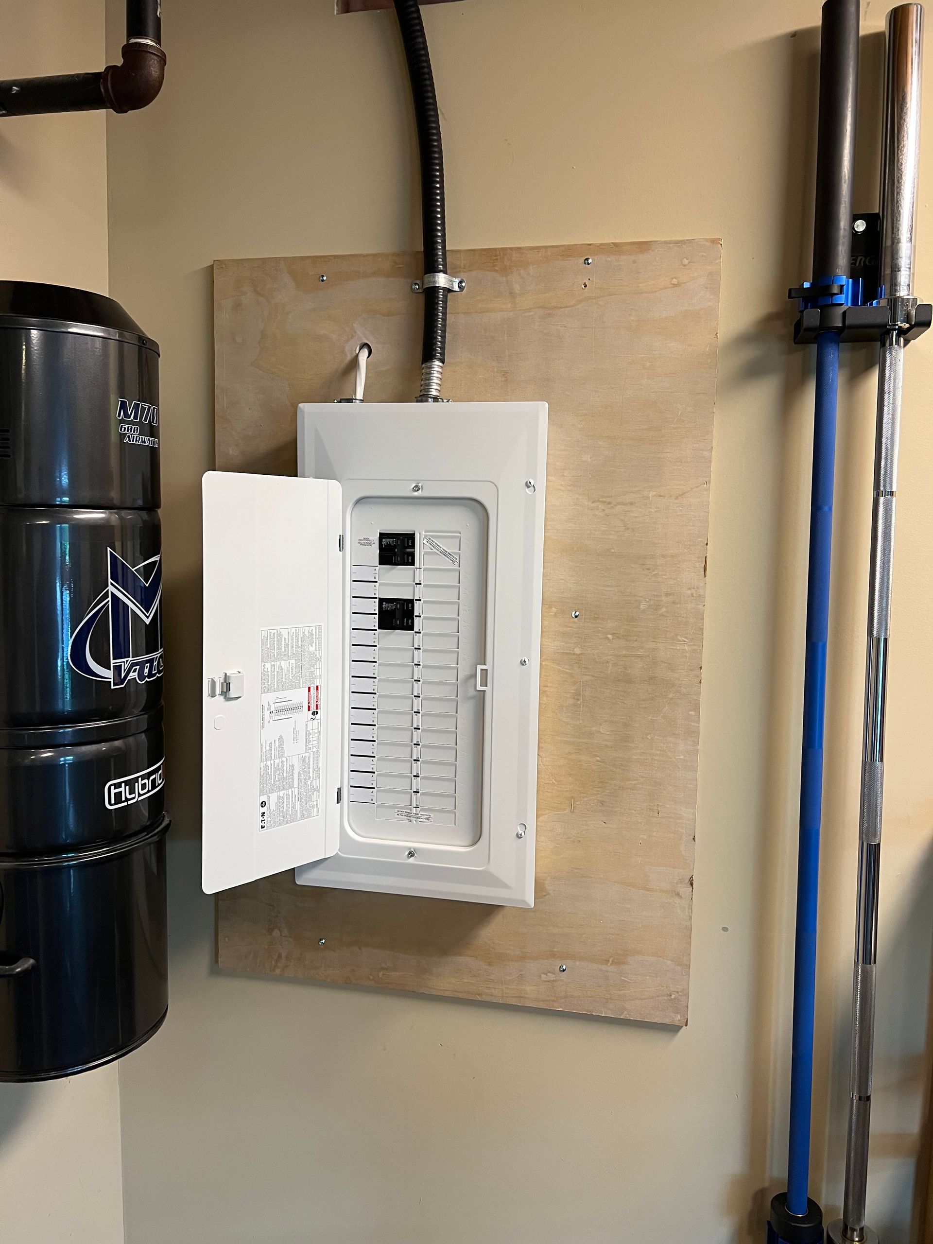 A electrical box is hanging on a wall next to a vacuum cleaner.