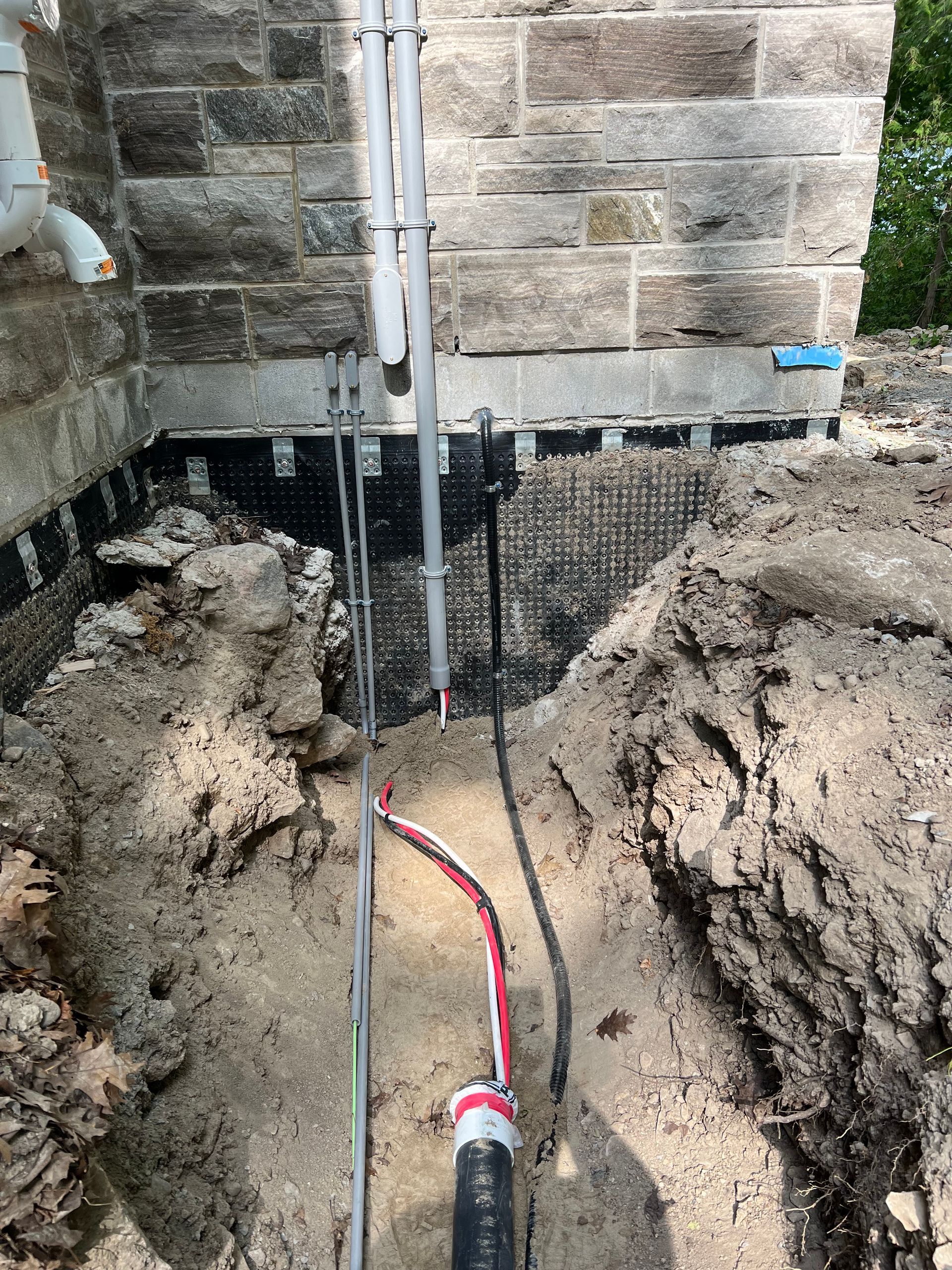 A pipe is being installed in the dirt next to a brick wall.
