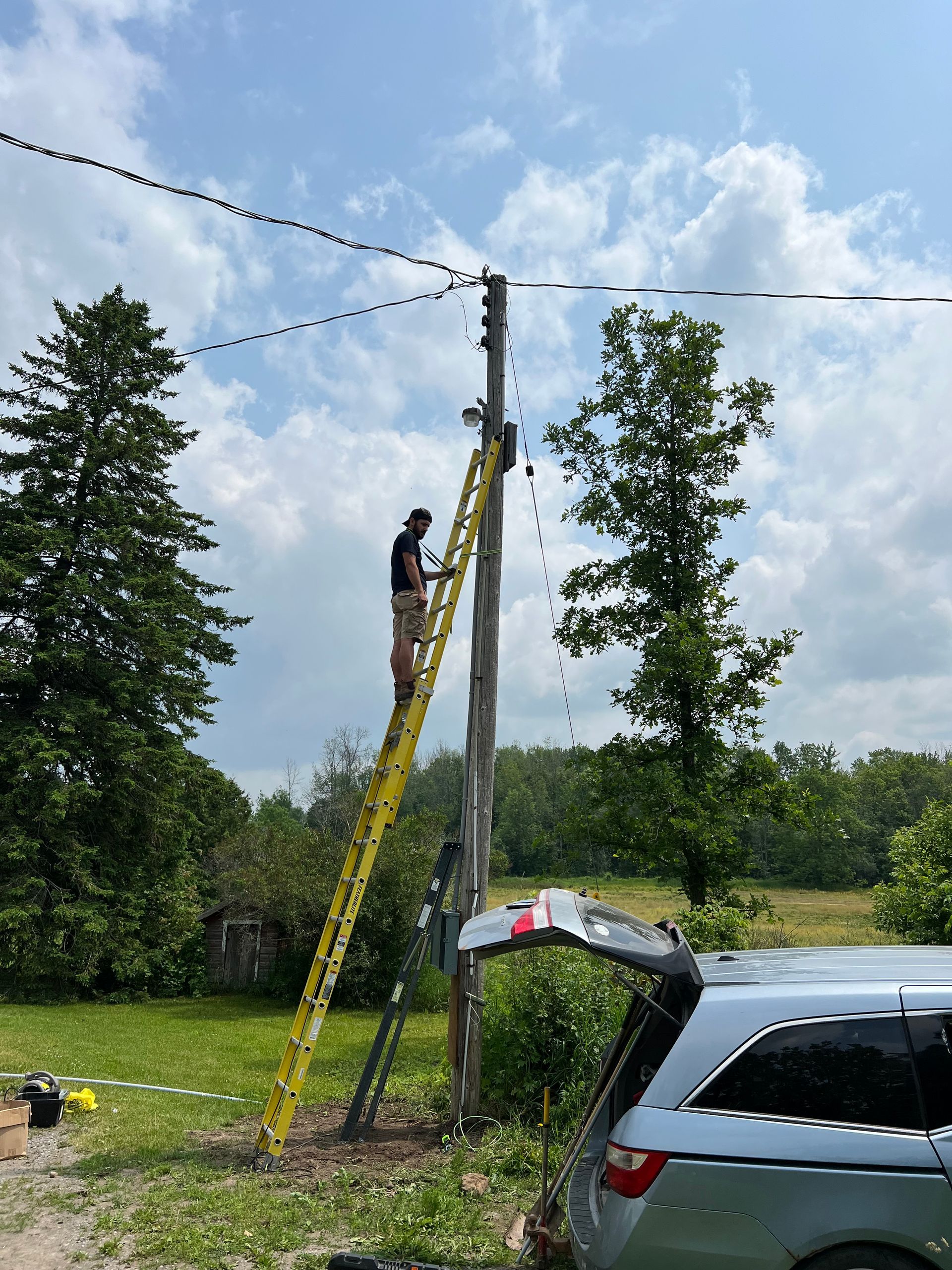 A man is standing on a ladder on top of a power pole.