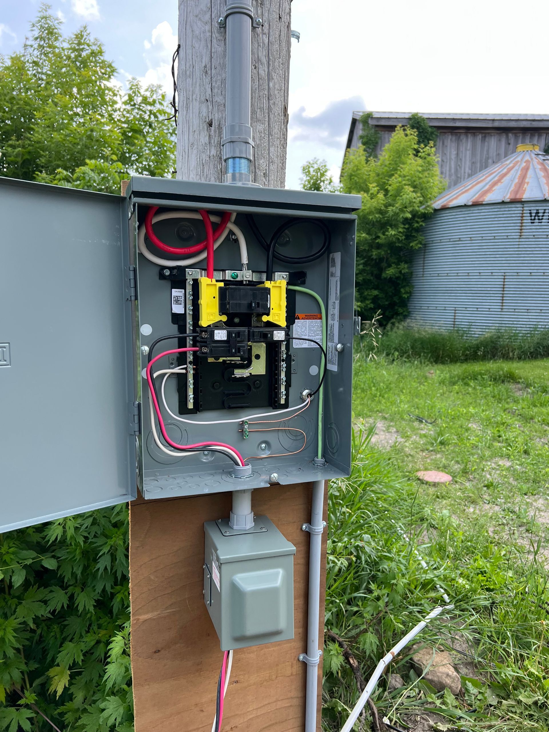 A electrical box is sitting on top of a wooden post in a field.