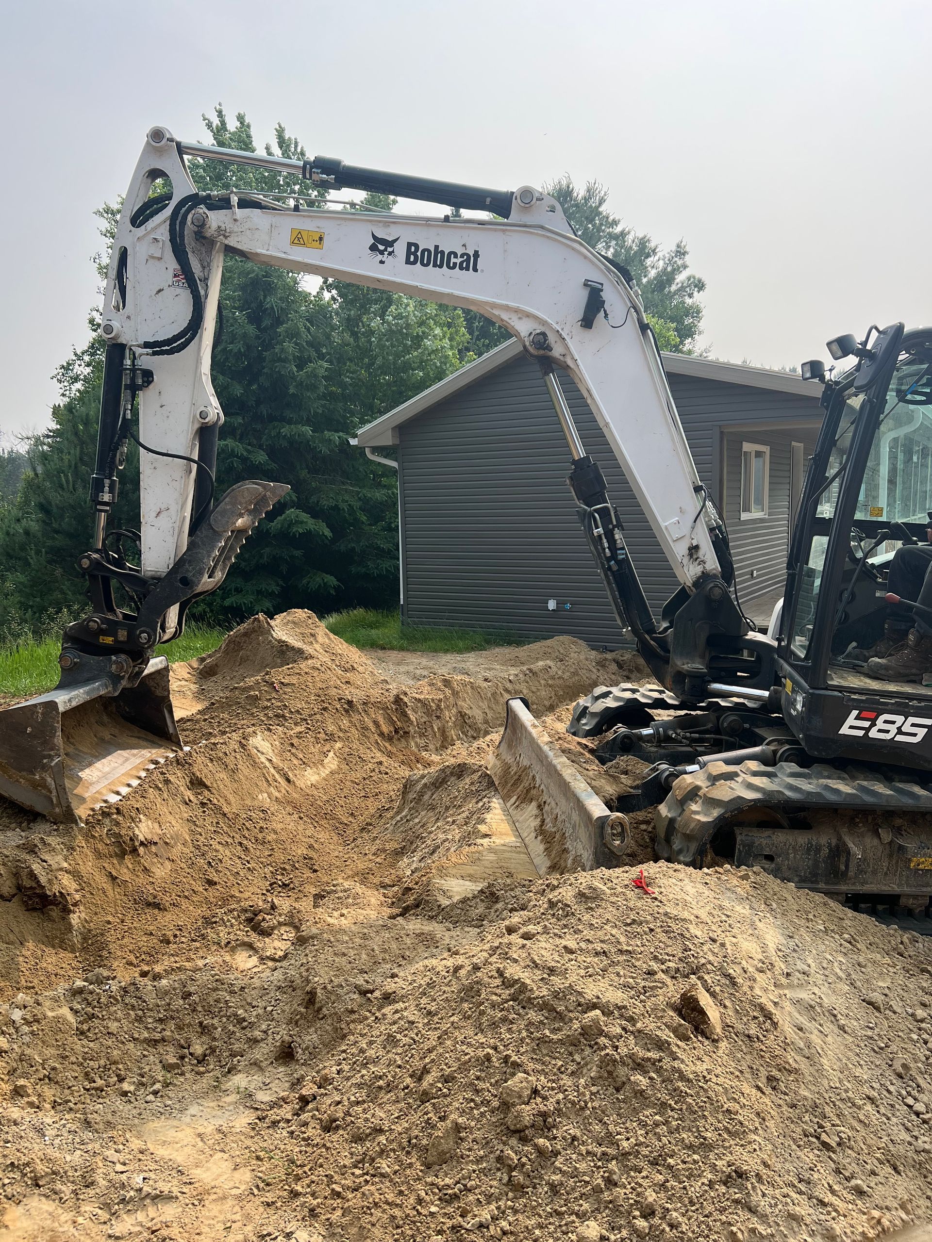 A bobcat excavator is digging a hole in the dirt in front of a house.