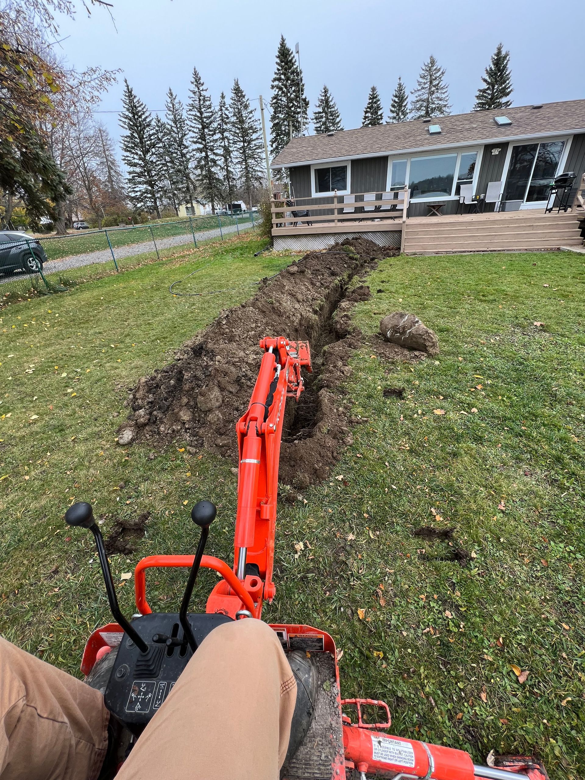 A person is driving a small red excavator in a yard.