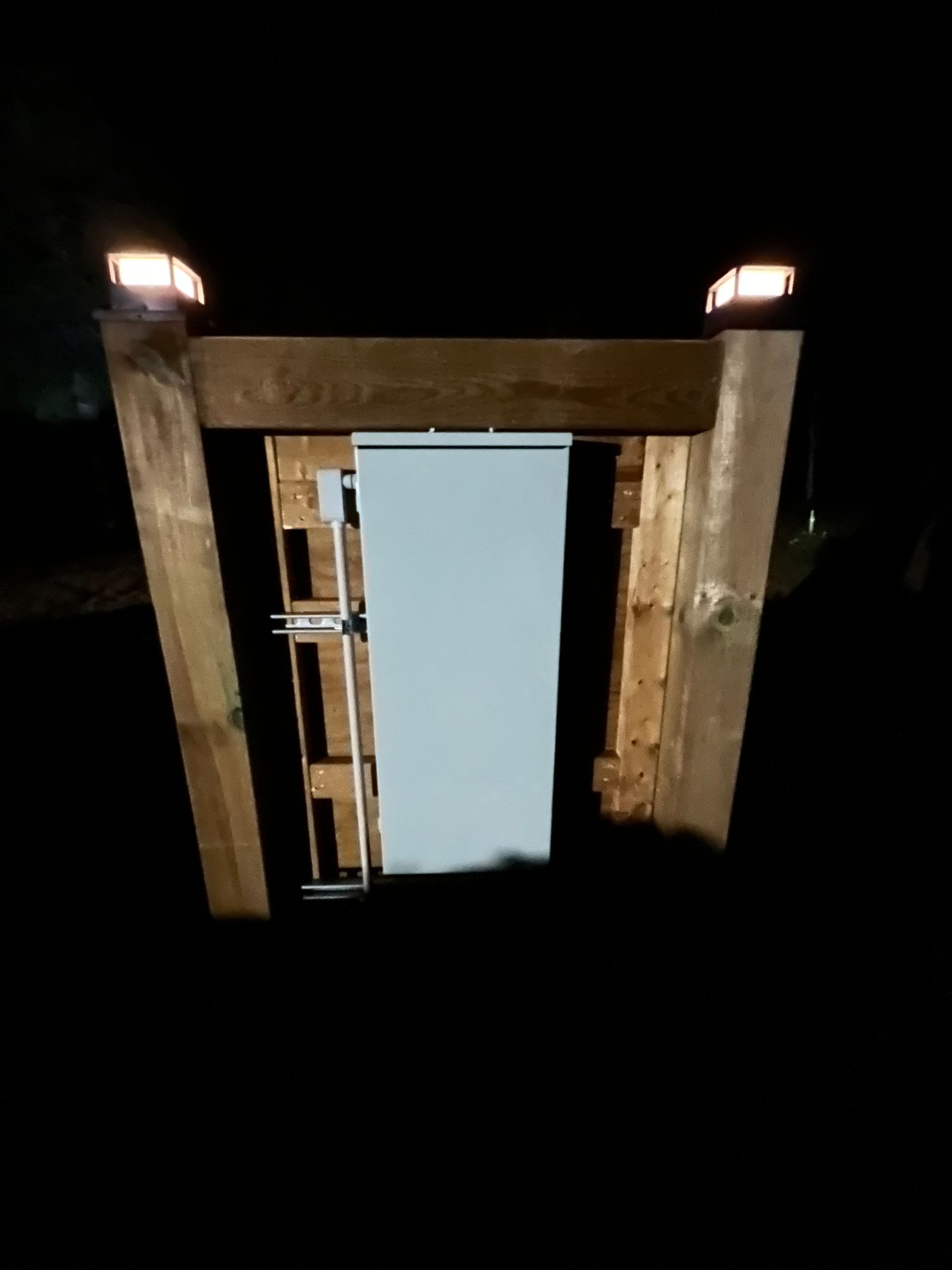 A white trash can is sitting inside of a wooden structure at night.