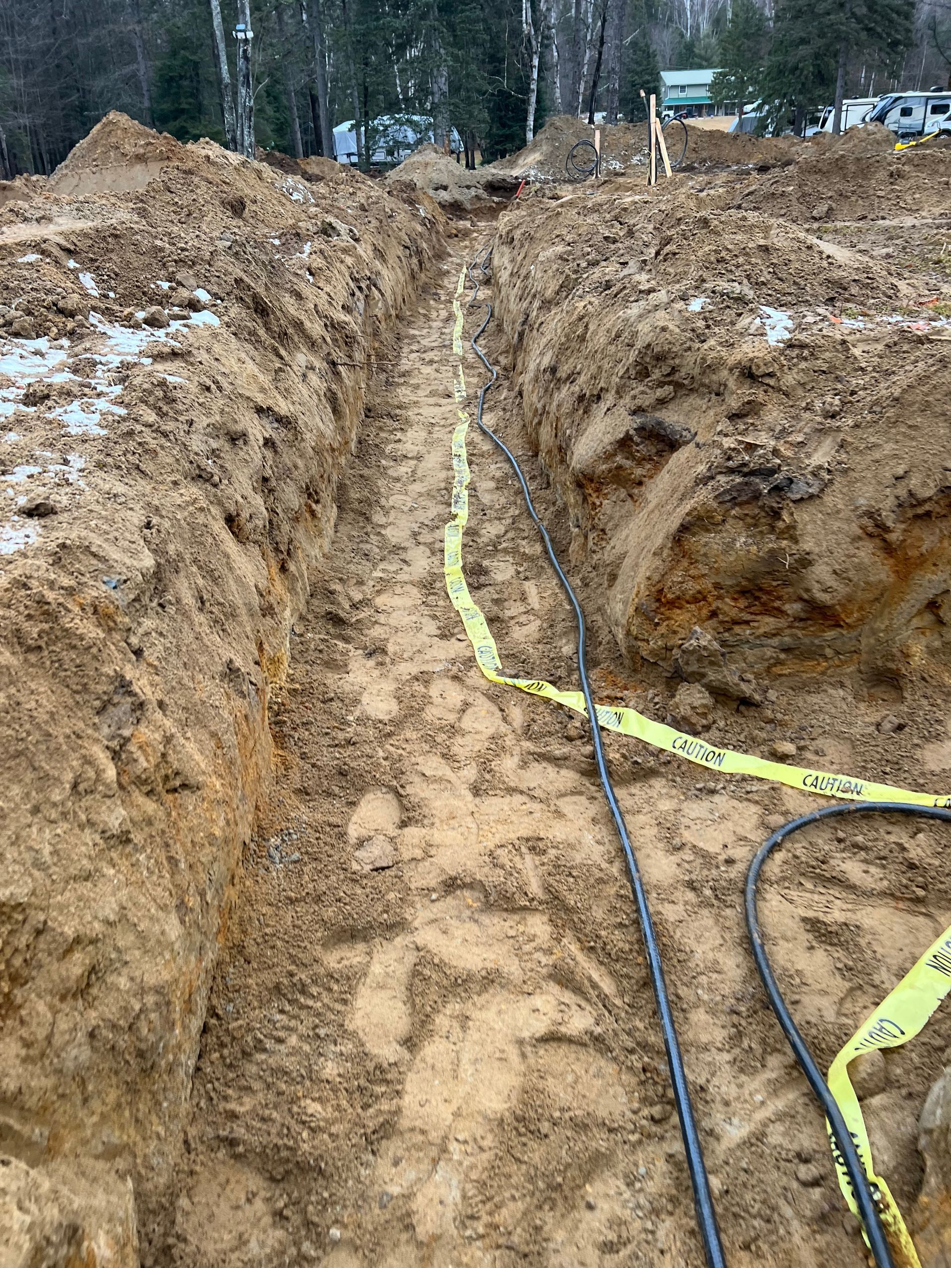 A bunch of wires are laying in the dirt in a trench.