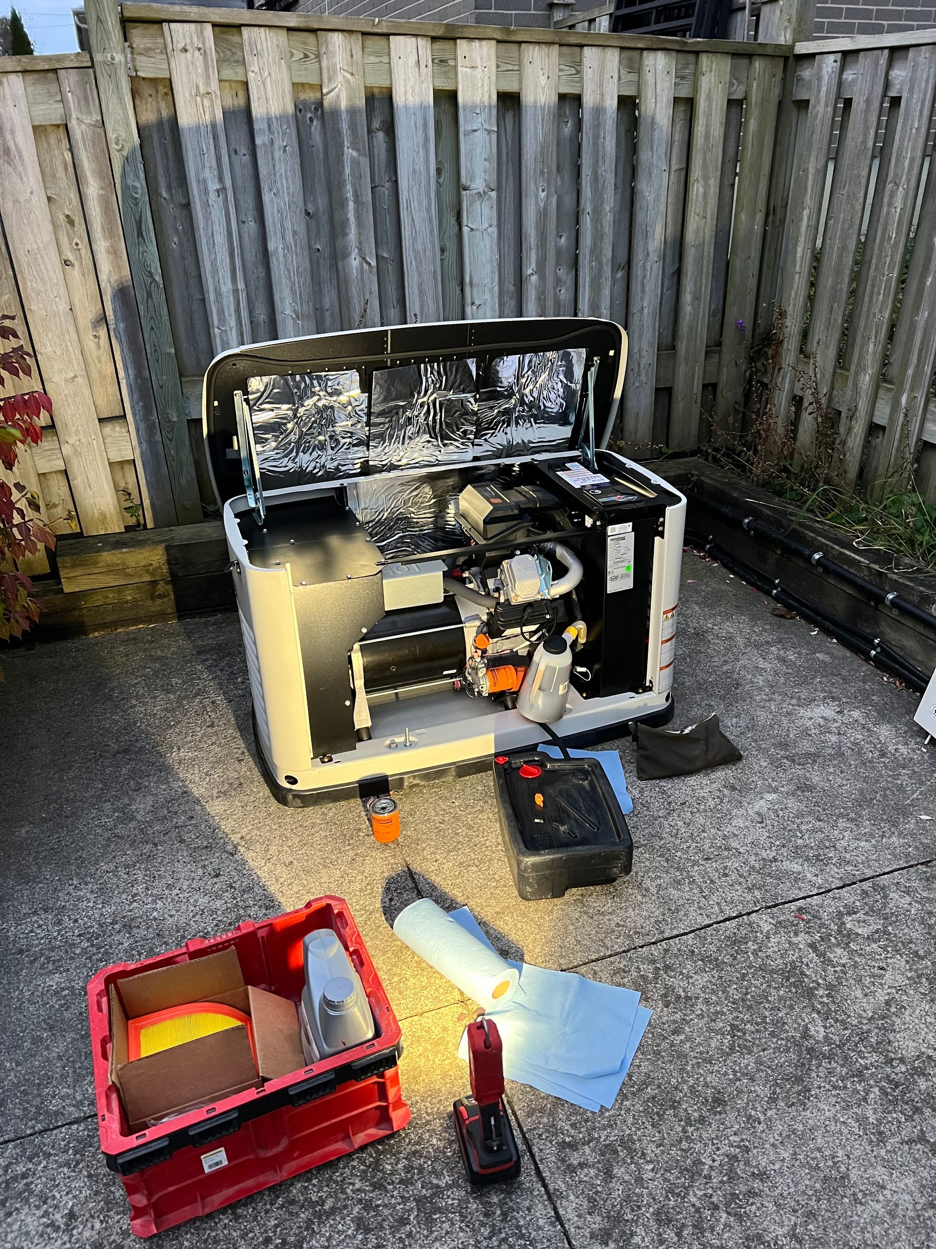 A generator is being repaired on a patio next to a wooden fence.