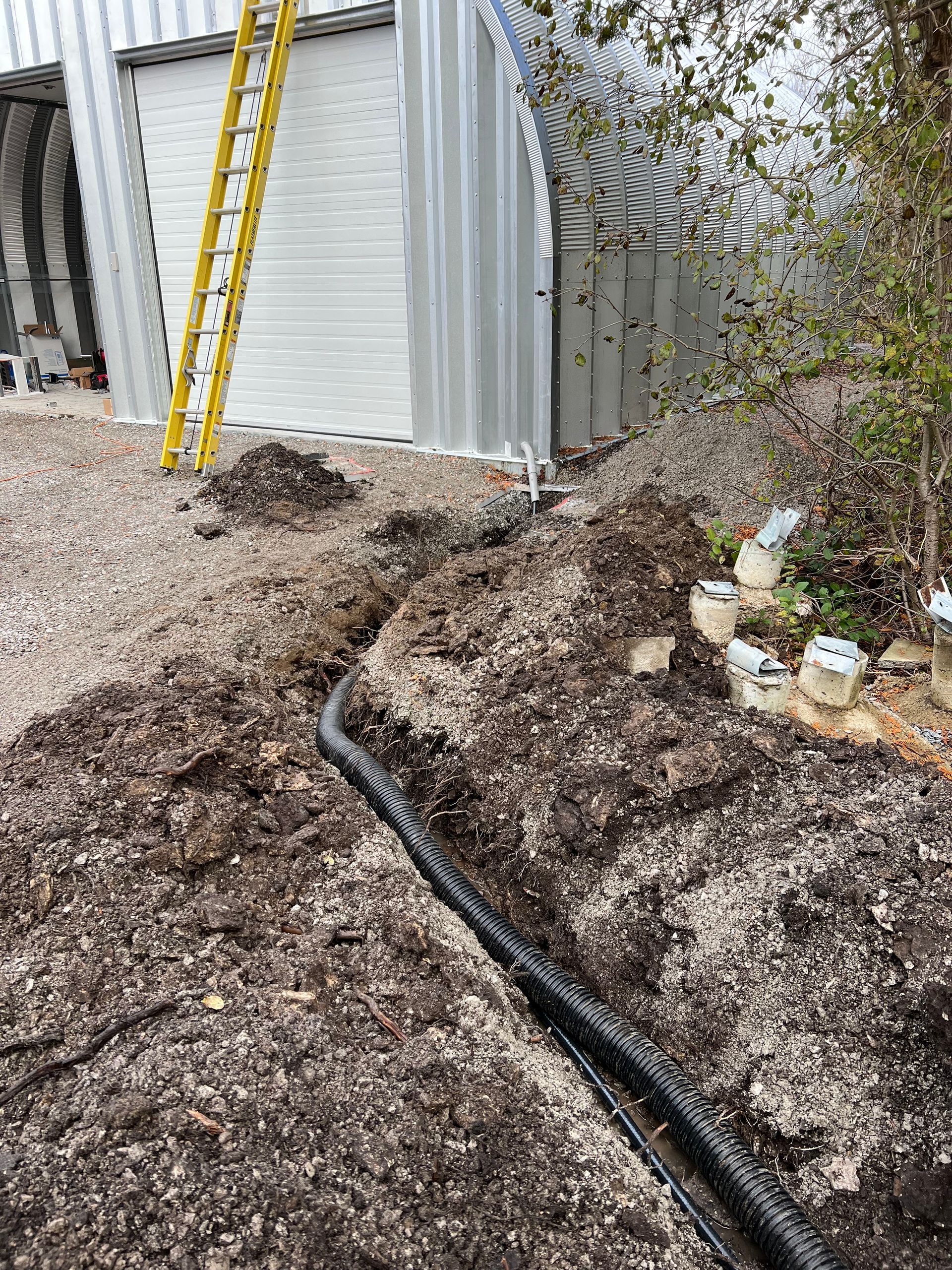 A black pipe is laying in the dirt next to a garage door.