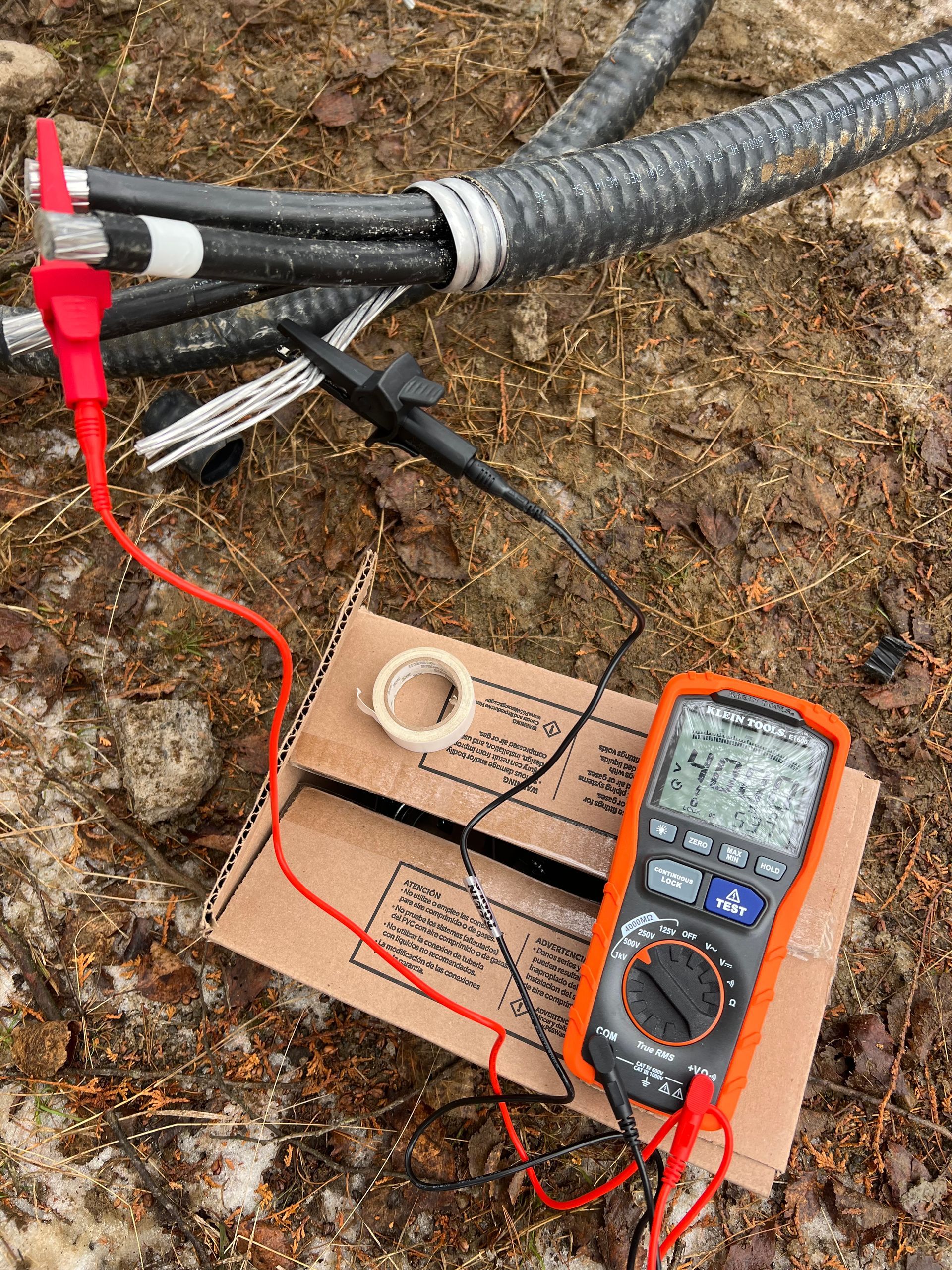 A multimeter is sitting on top of a cardboard box next to a bunch of wires.