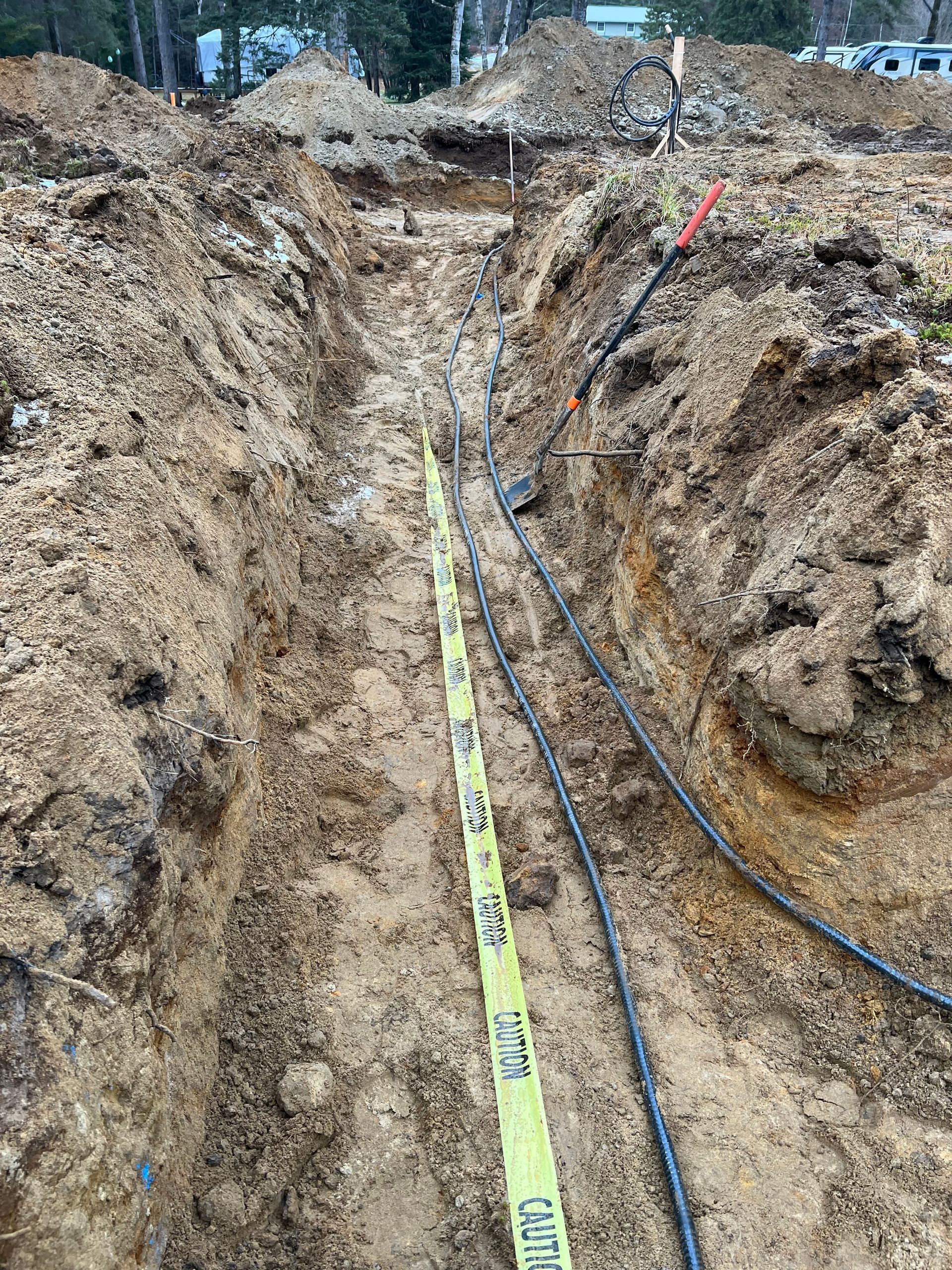 A bunch of wires are laying in the dirt in a trench.