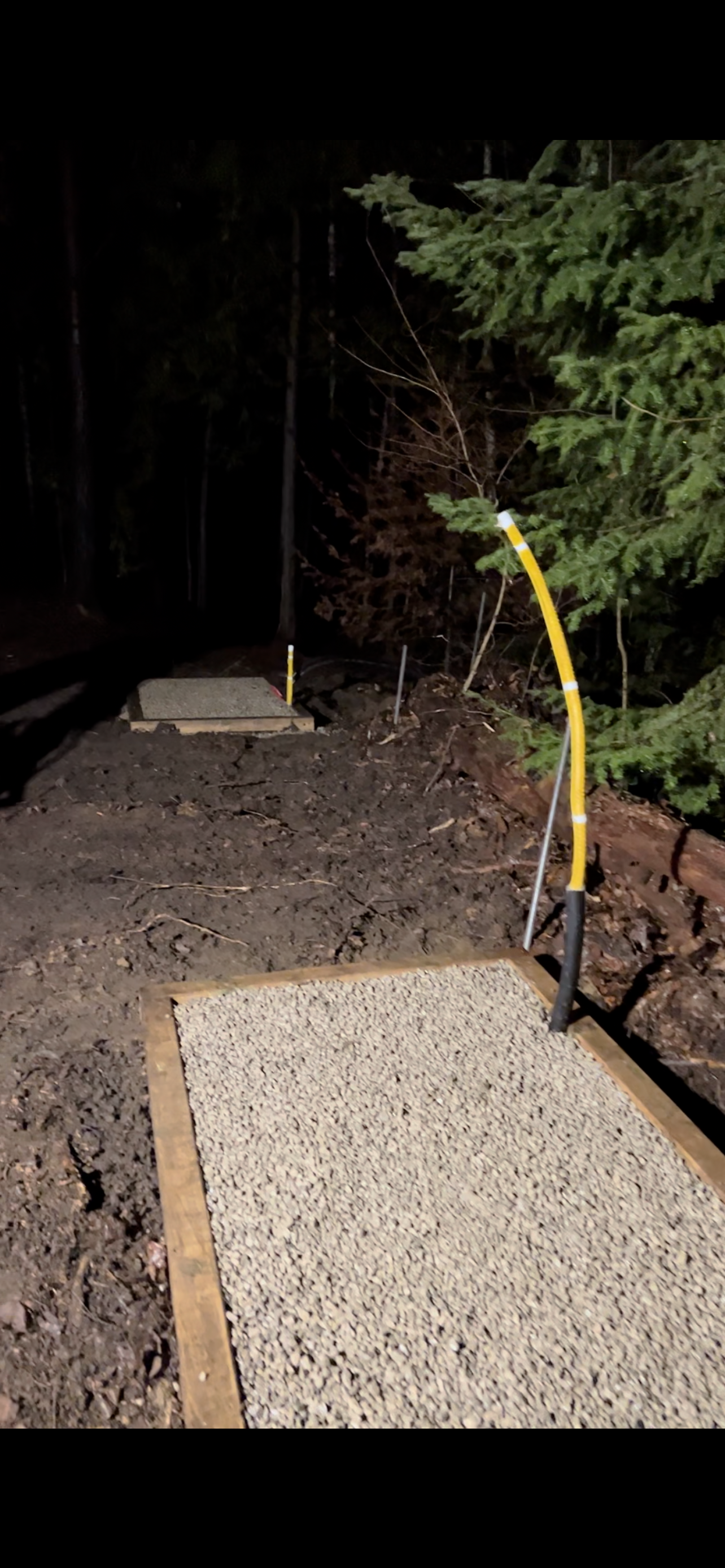A yellow hose is attached to a gravel area in the woods.