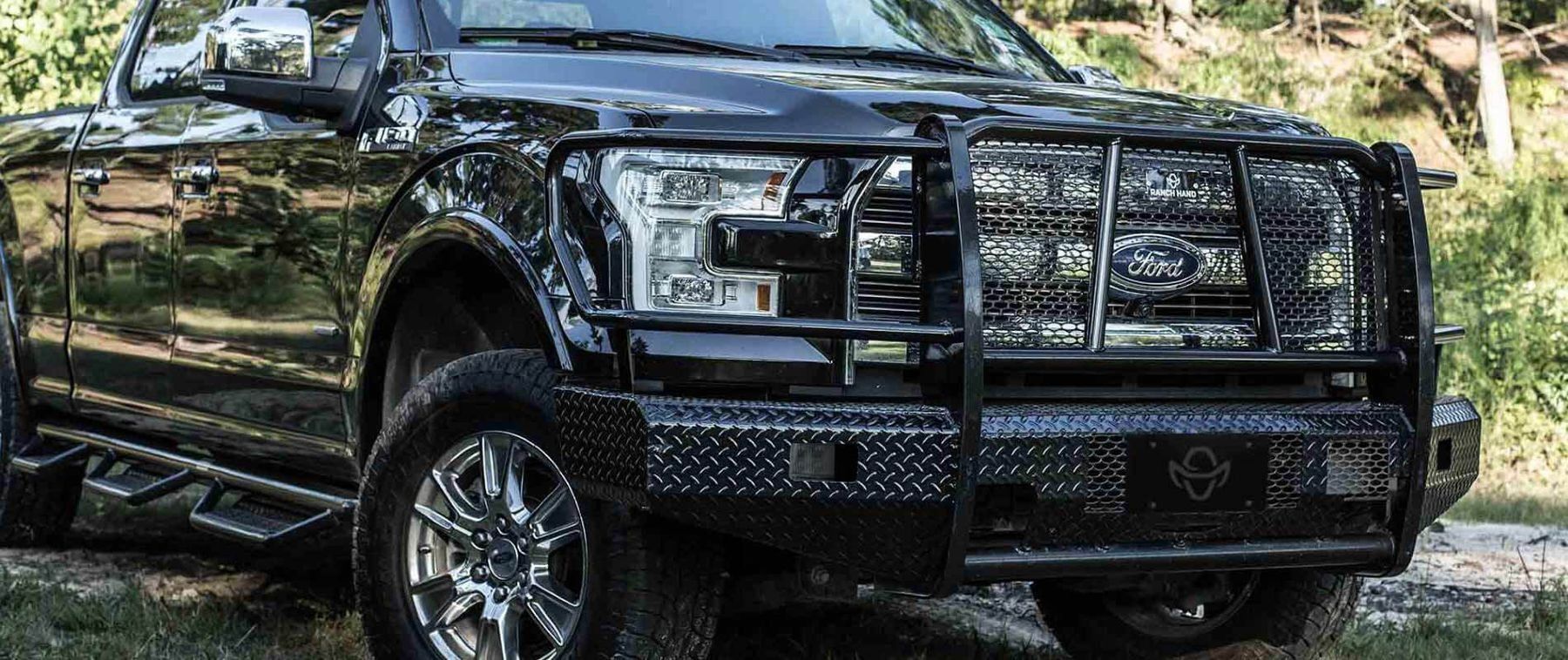 Black pickup truck with a heavy-duty grille parked outdoors in a wooded area