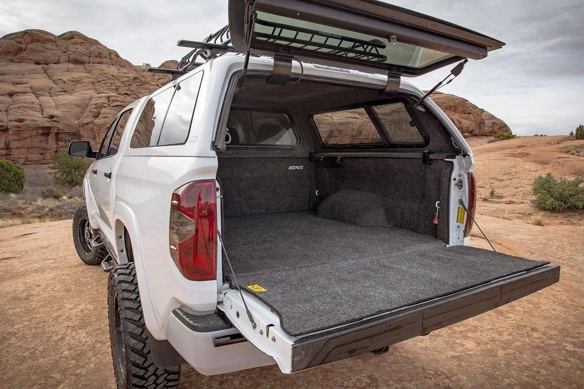 White SUV with rear hatch open, showing an extended cargo platform in a rocky desert setting