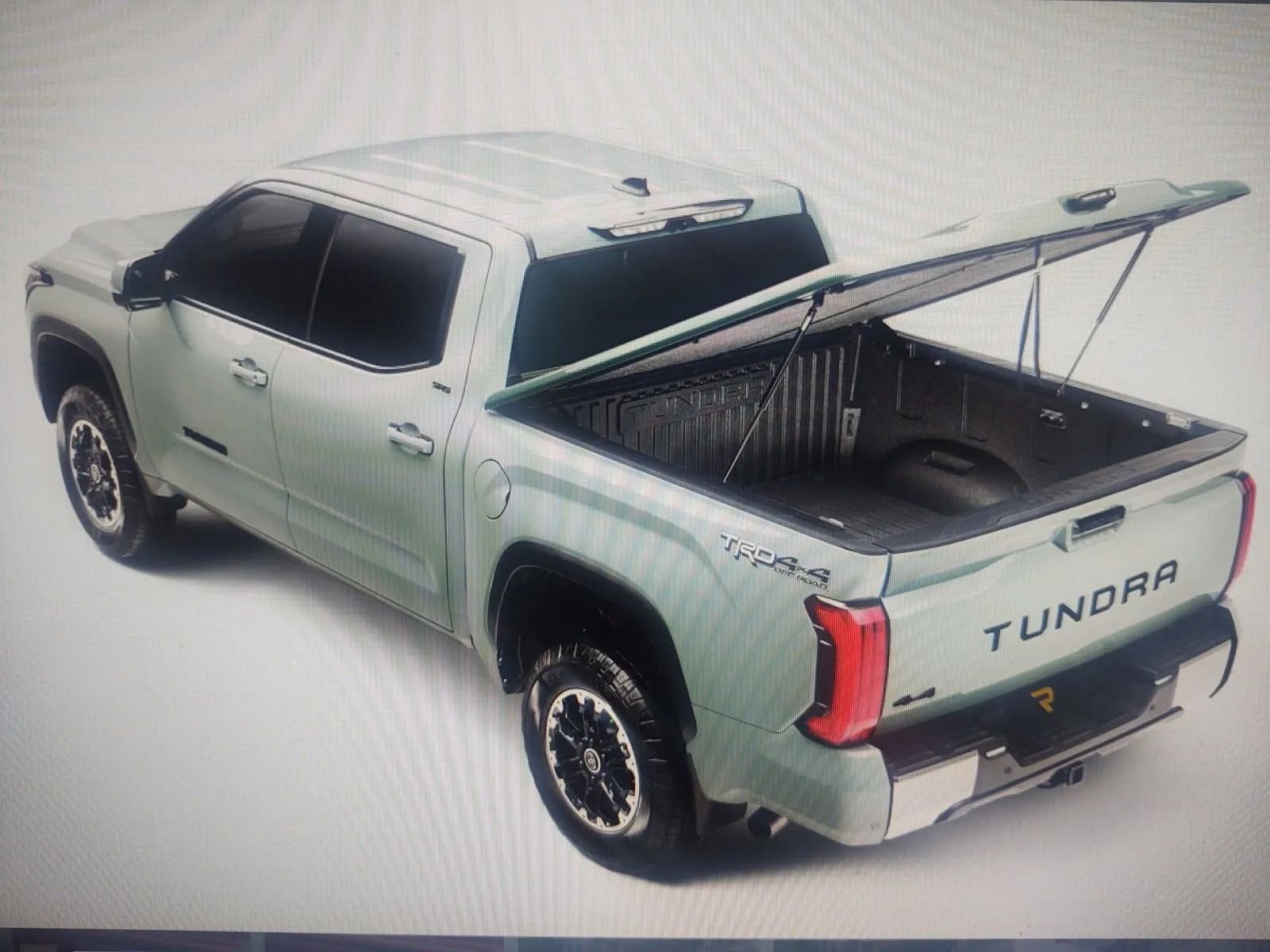 Light green Toyota Tundra pickup with open bed tonneau cover, shown in three-quarter rear view