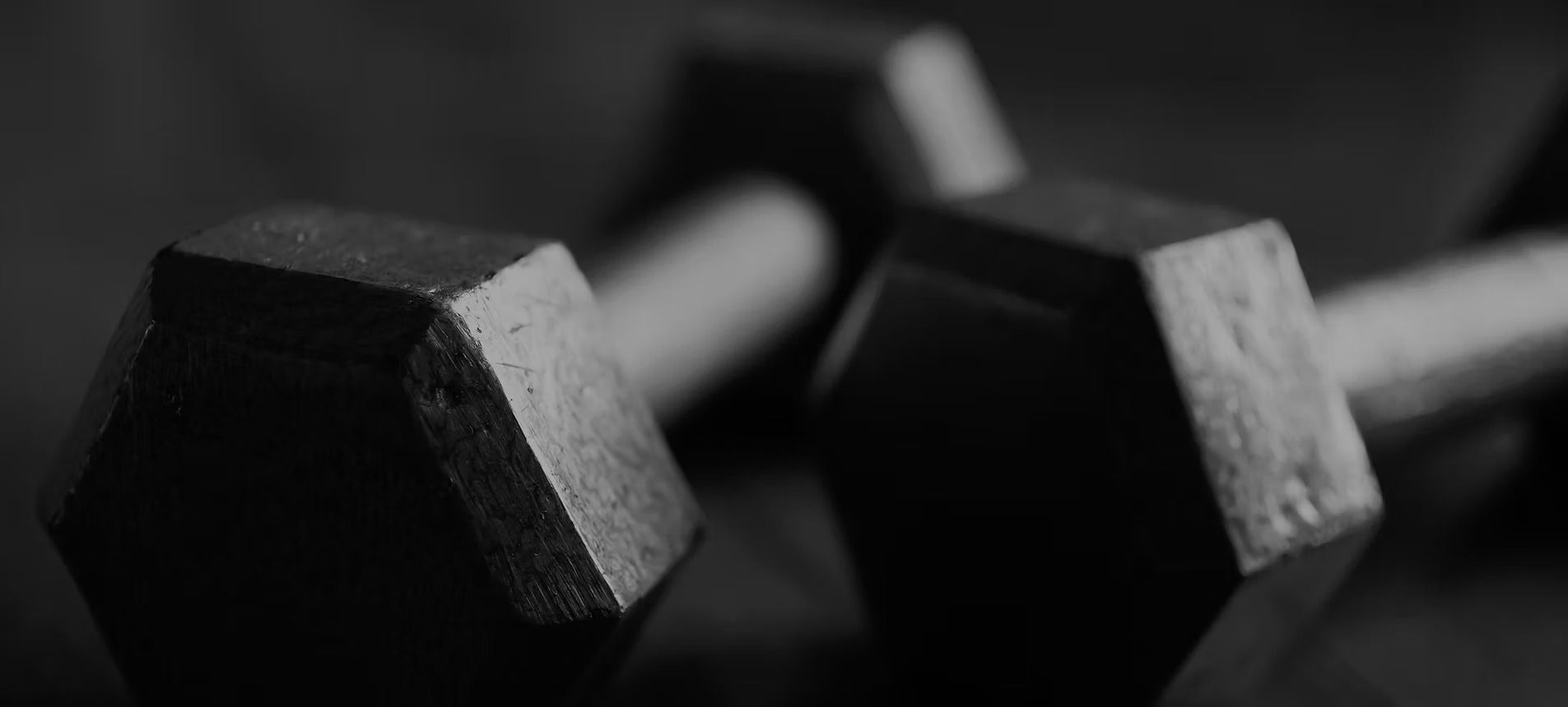 Black and white photo of two dumbbells on a surface, one in focus.