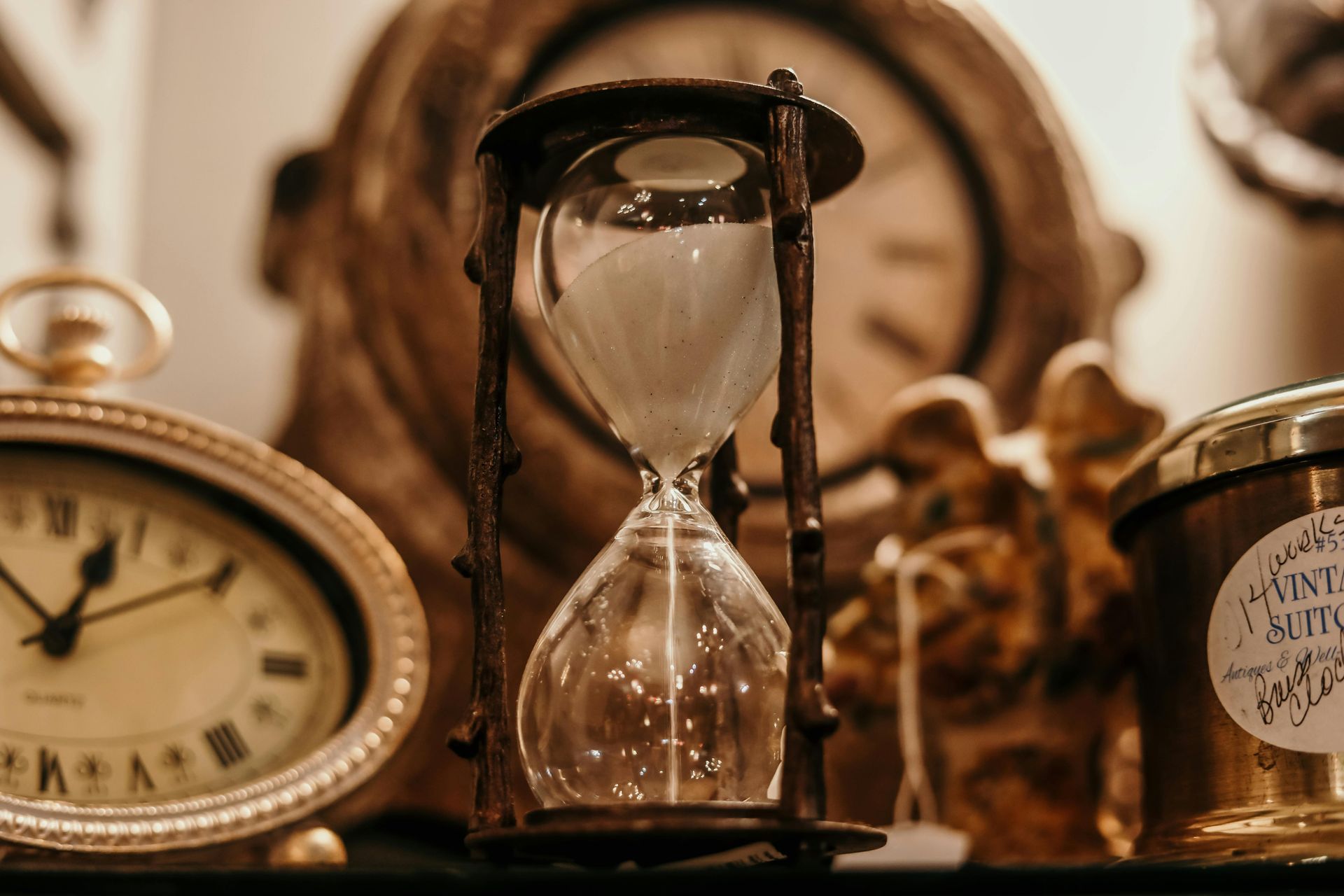 Hourglass with sand trickling down, surrounded by antique clocks.