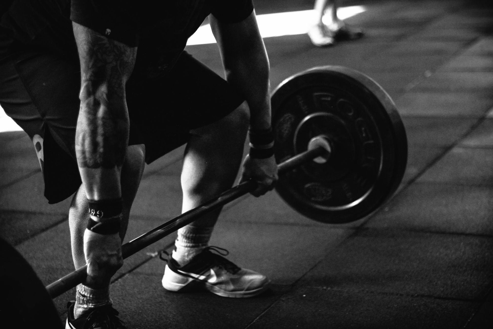 Person lifting a barbell with weight plates at a gym. Black and white photo.
