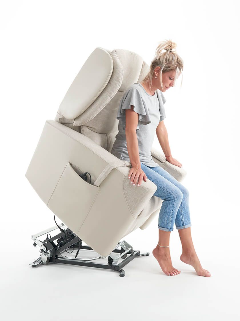 Donna seduta su una poltrona elevatrice beige, che si alza in posizione eretta. Sfondo bianco.