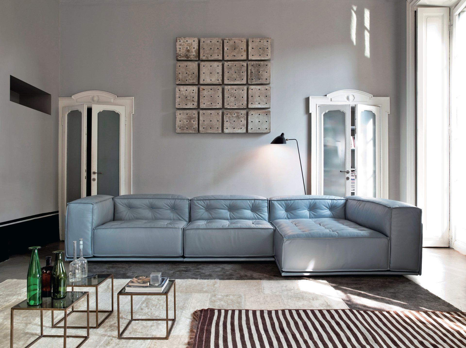 Un soggiorno moderno con un divano componibile blu, quadri decorativi alle pareti e tavolini in vetro su un tappeto a fantasia.