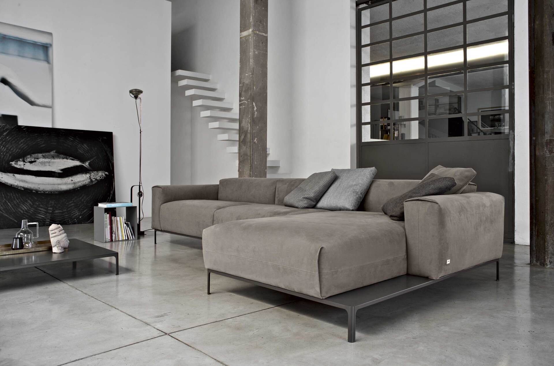 Soggiorno moderno con divano componibile grigio, pavimento in cemento ed elementi in stile industriale.