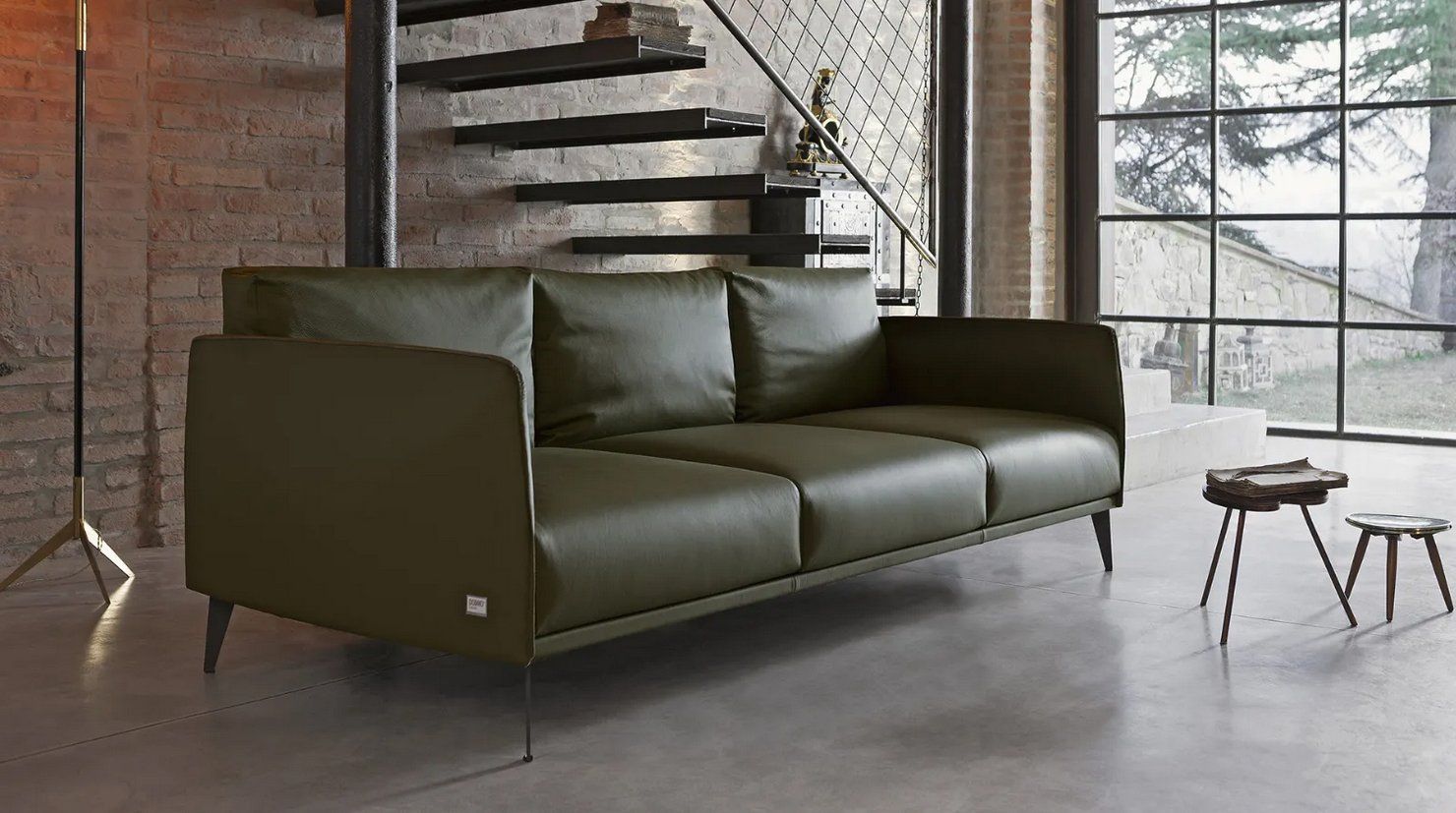 Divano in pelle verde in un moderno loft con parete in mattoni e scale.