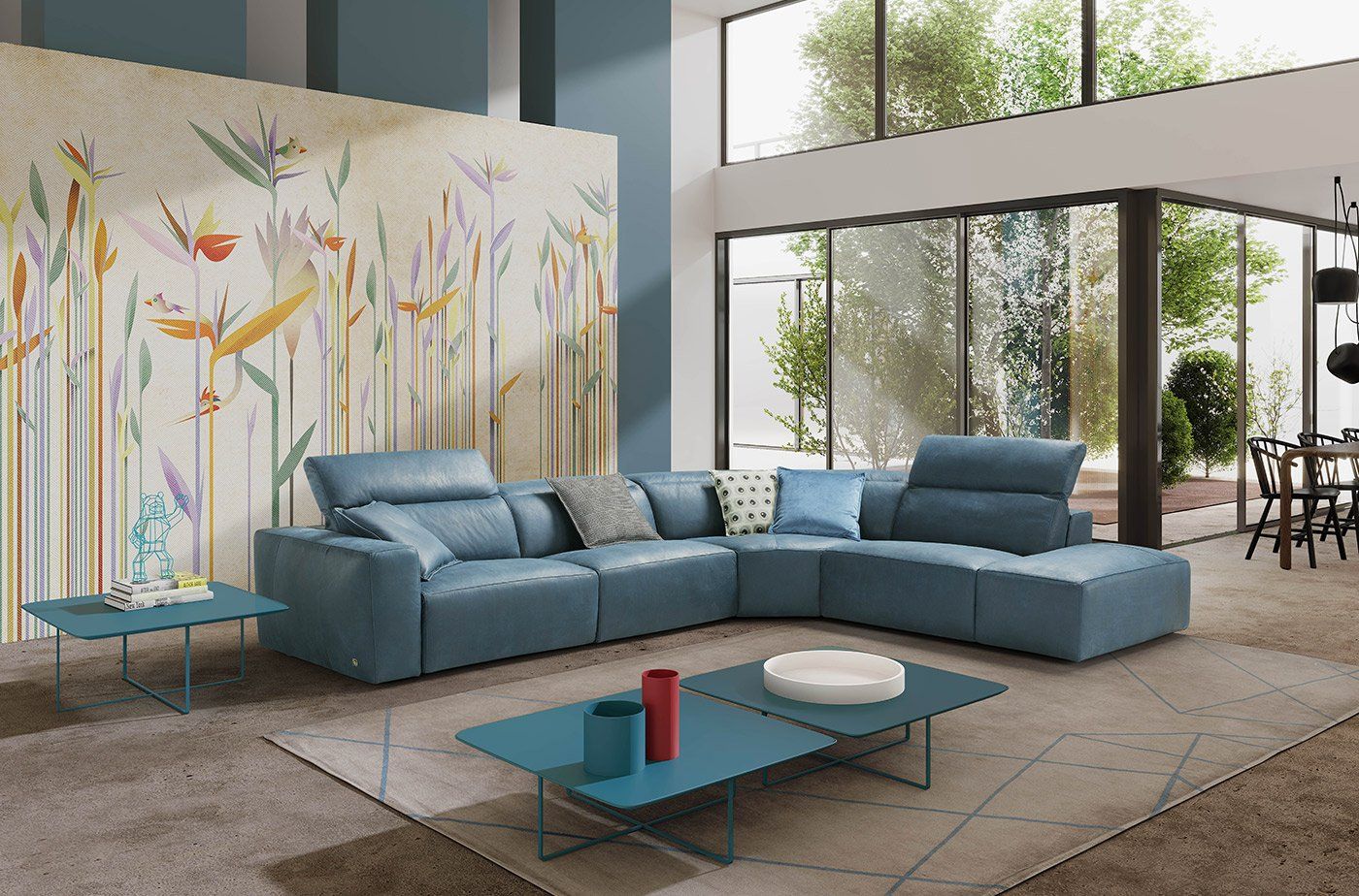 Divano componibile blu in un soggiorno moderno con murale floreale e ampie finestre.