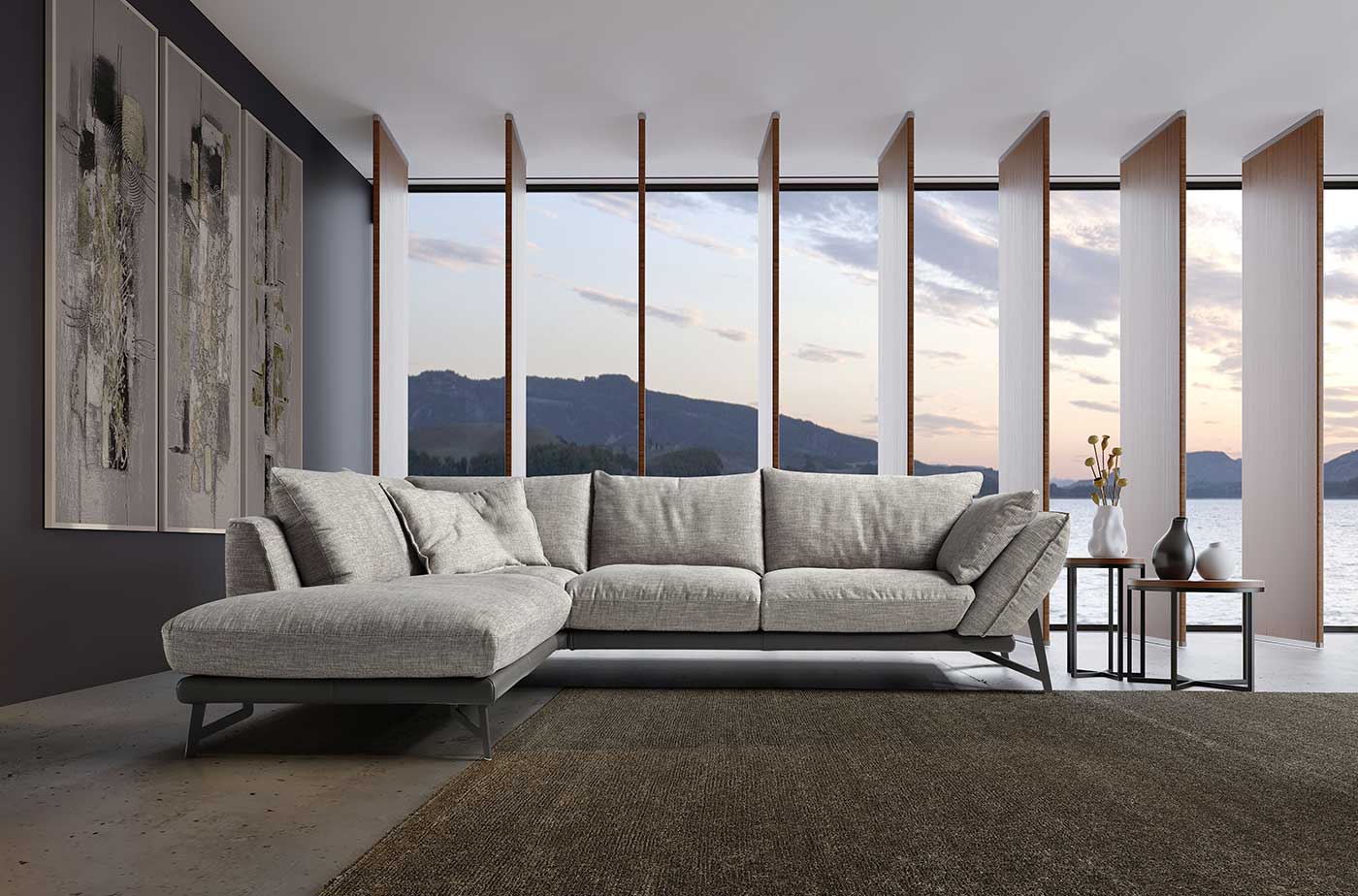 Divano grigio a L in un soggiorno moderno con ampie finestre che si affacciano sul lago e sulle montagne.