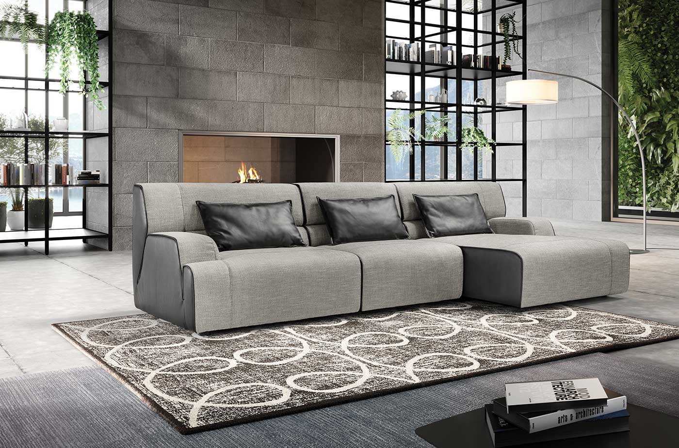 Divano componibile moderno grigio con cuscini grigio scuro e pouf su un tappeto a fantasia in una stanza con camino.