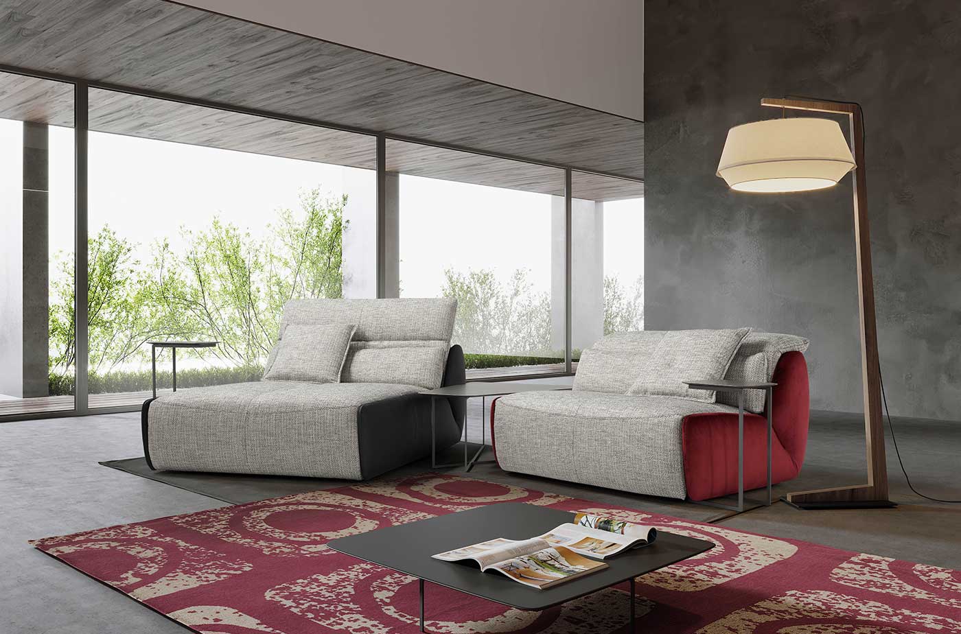 Due poltrone moderne con tavolini laterali in una stanza con grandi finestre, tappeto rosso, lampada da terra.