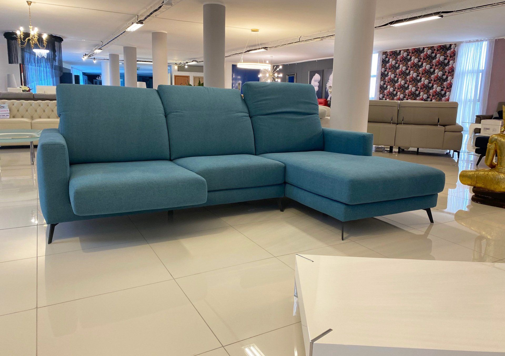 Divano componibile blu in uno showroom con pavimenti e colonne bianchi.