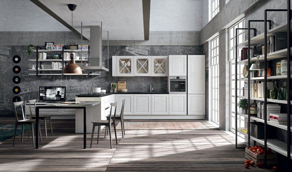 Cucina moderna con mobili bianchi, ripiani scuri e scaffali aperti contro una parete di mattoni grigi.