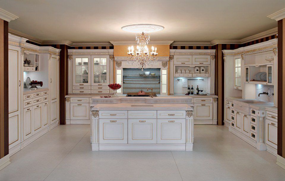 Elegante cucina bianca classica con mobili decorati, isola e lampadario.