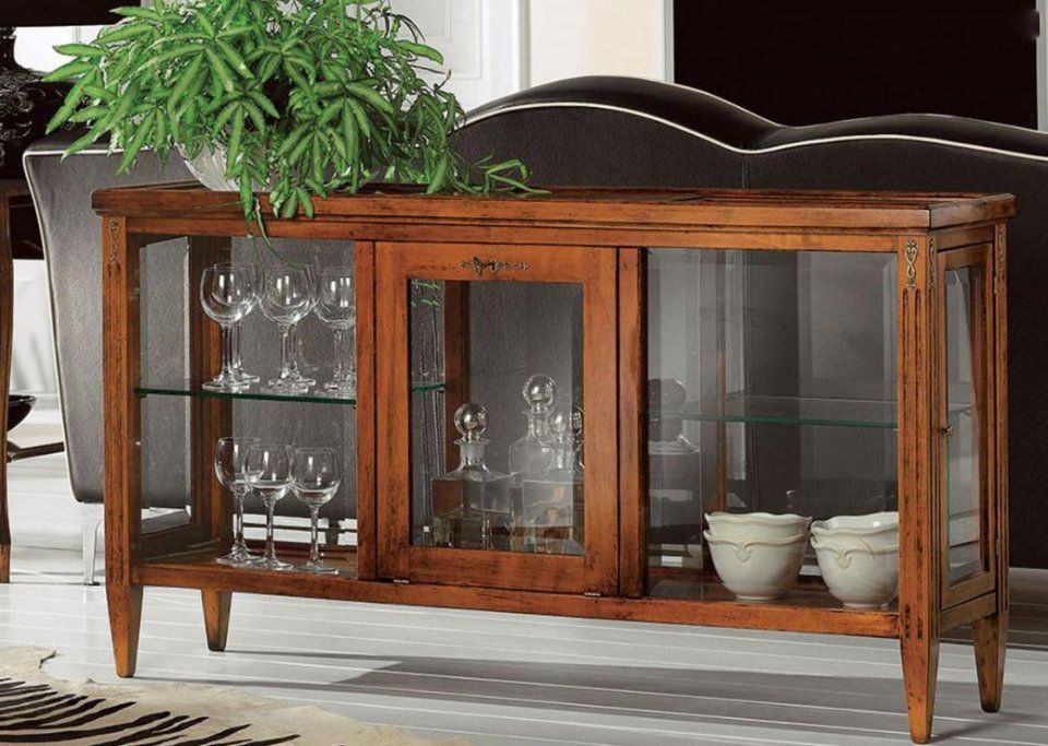 Vetrina in legno con ante in vetro, contenente oggetti in vetro e ciotole decorative; sormontata da una pianta in vaso.